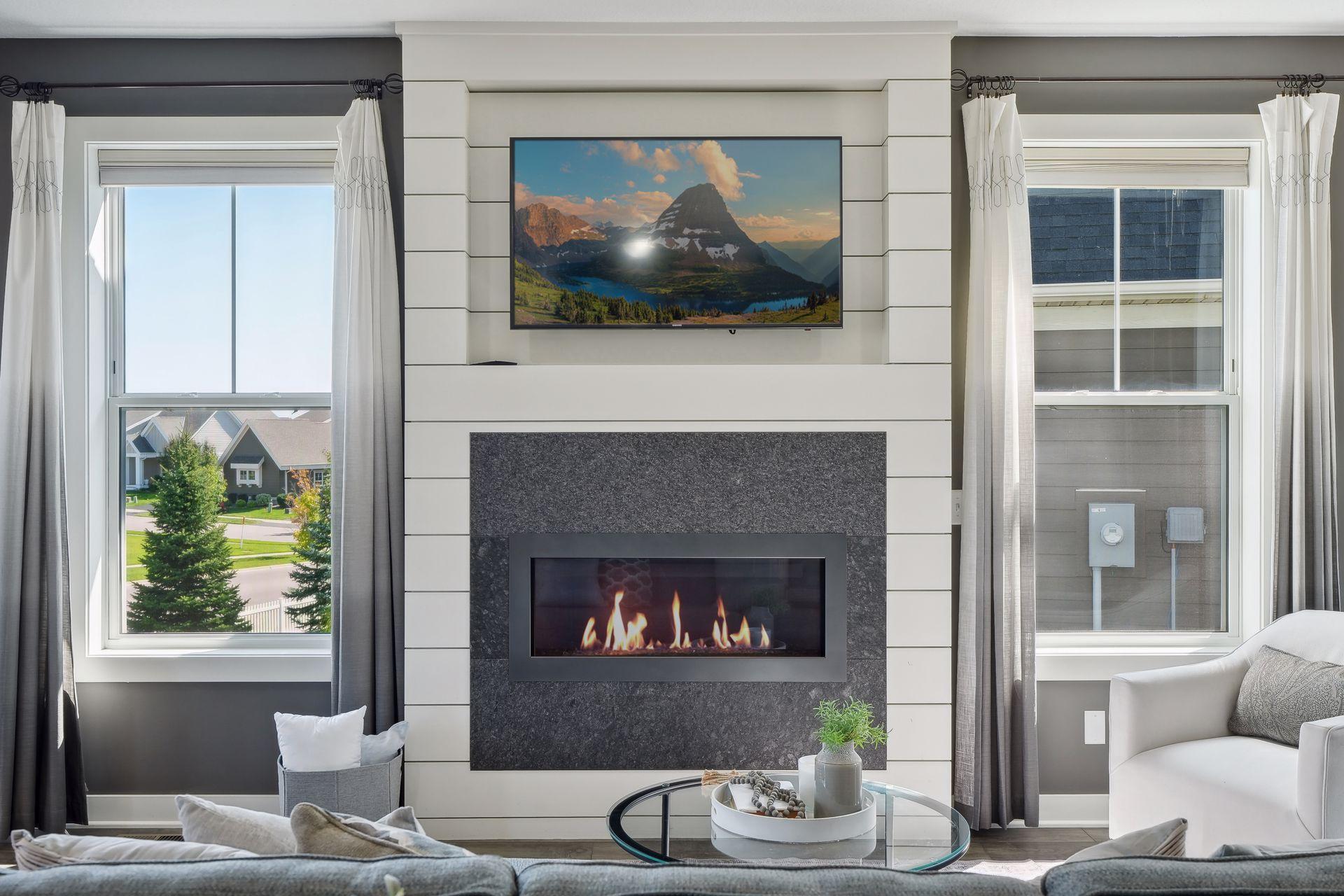 Living room with a gas fireplace in a dark stone surround, flanked by tall curtained windows.