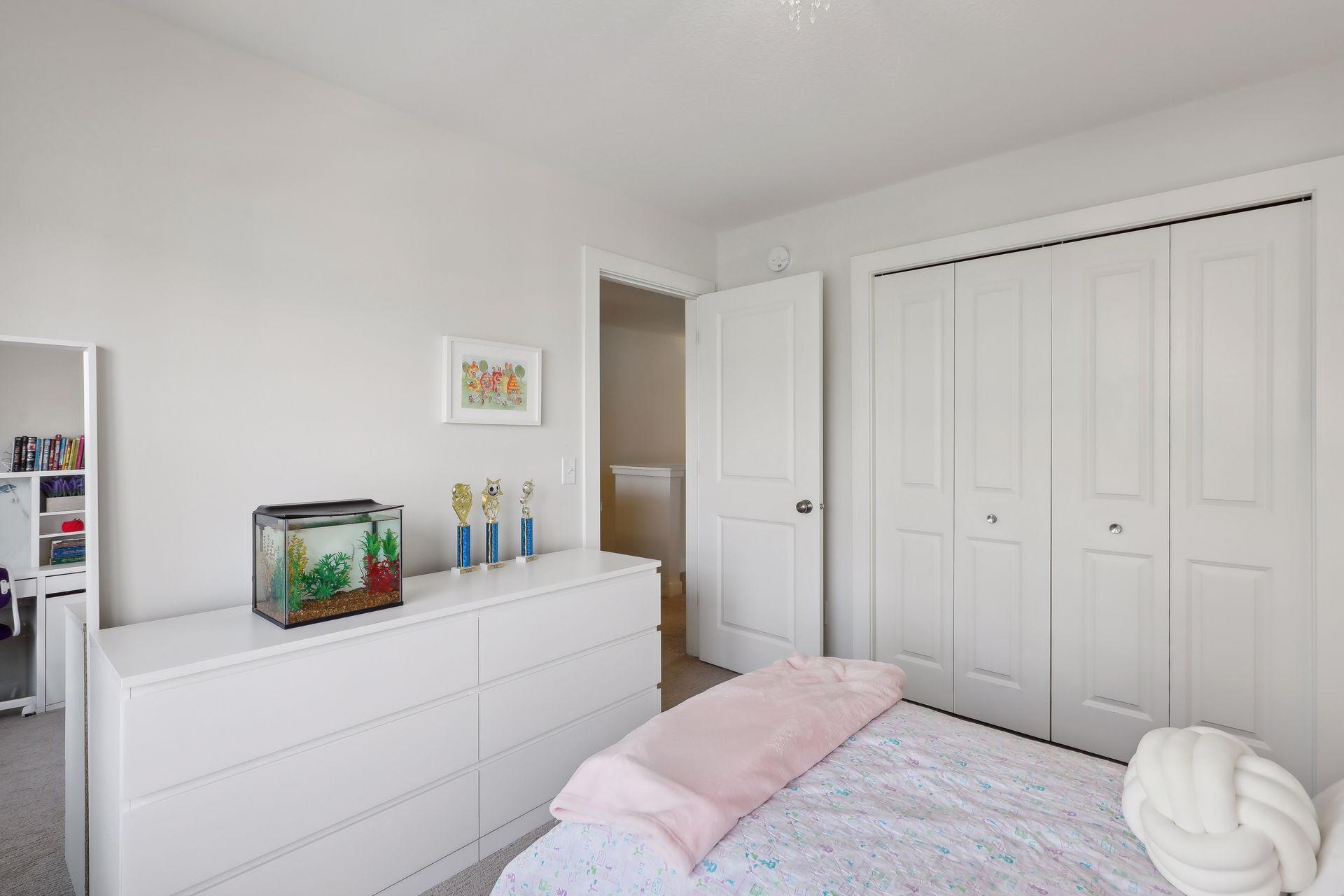 Bedroom with a white dresser, aquarium, and trophies beside a bed with pink bedding.