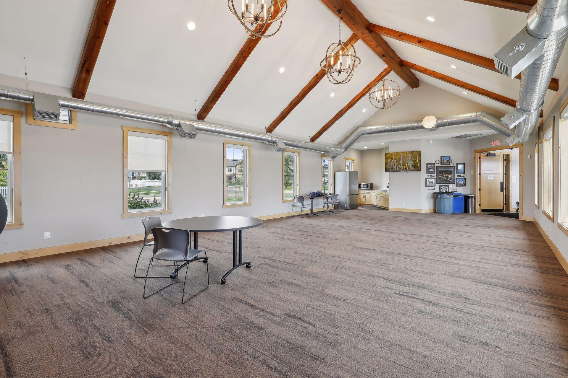 Spacious community room with vaulted wood-beamed ceiling, kitchenette, and open floor area.