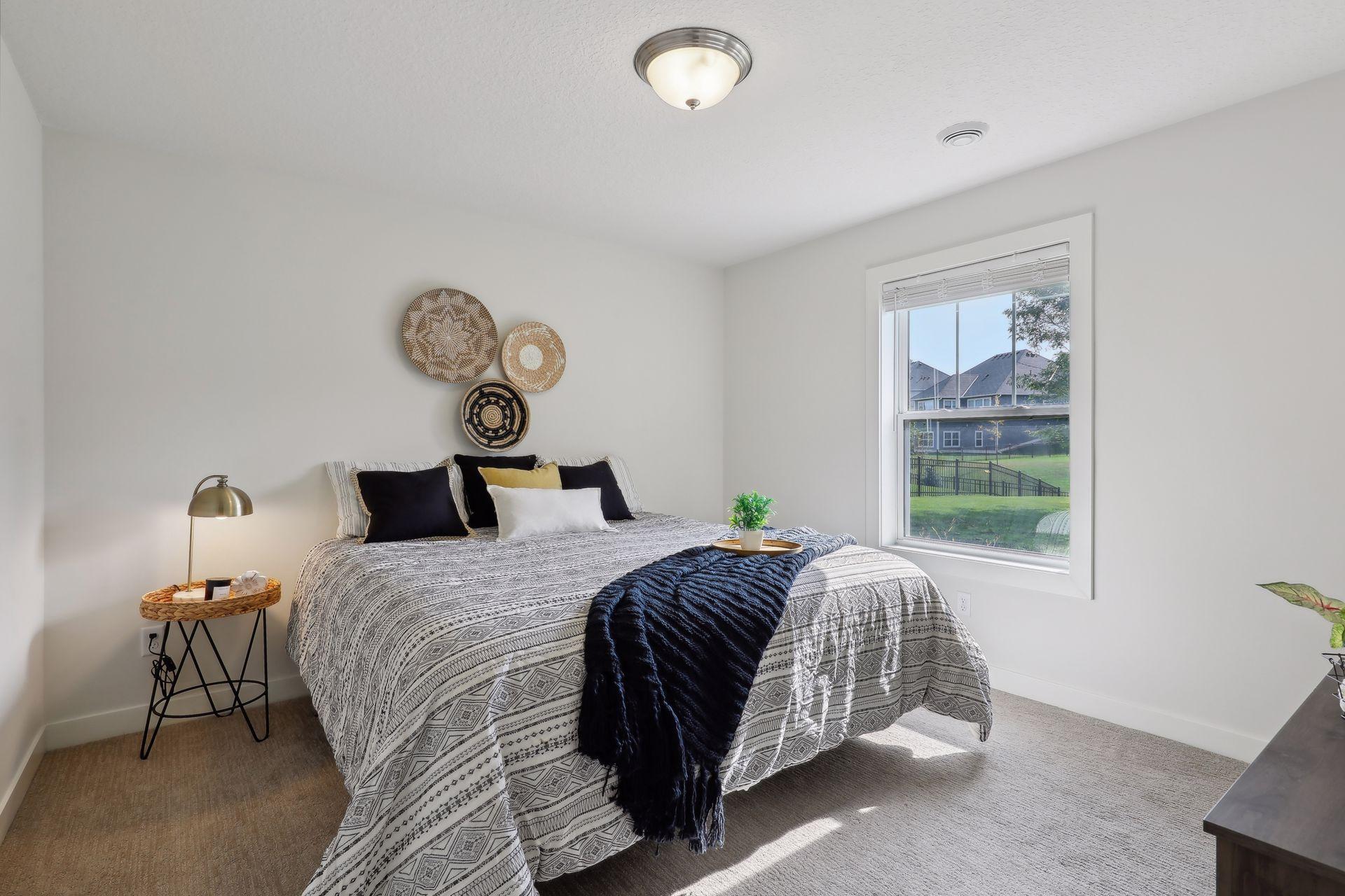Staged bedroom with patterned bedding, woven wall decor, and a window overlooking the fenced yard.
