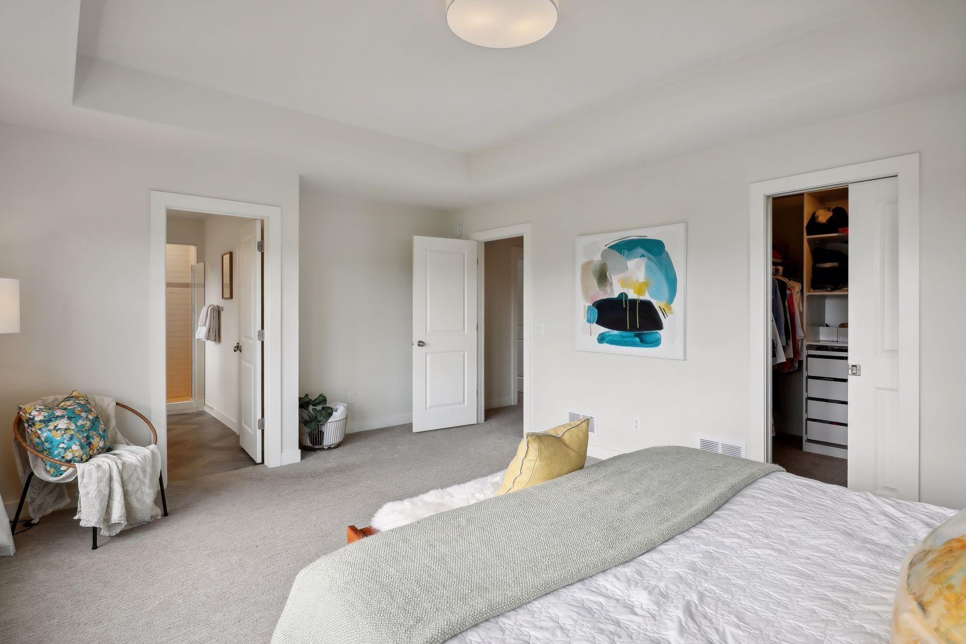 Bedroom with light carpet, abstract wall art, and open ensuite bathroom and walk-in closet doors.