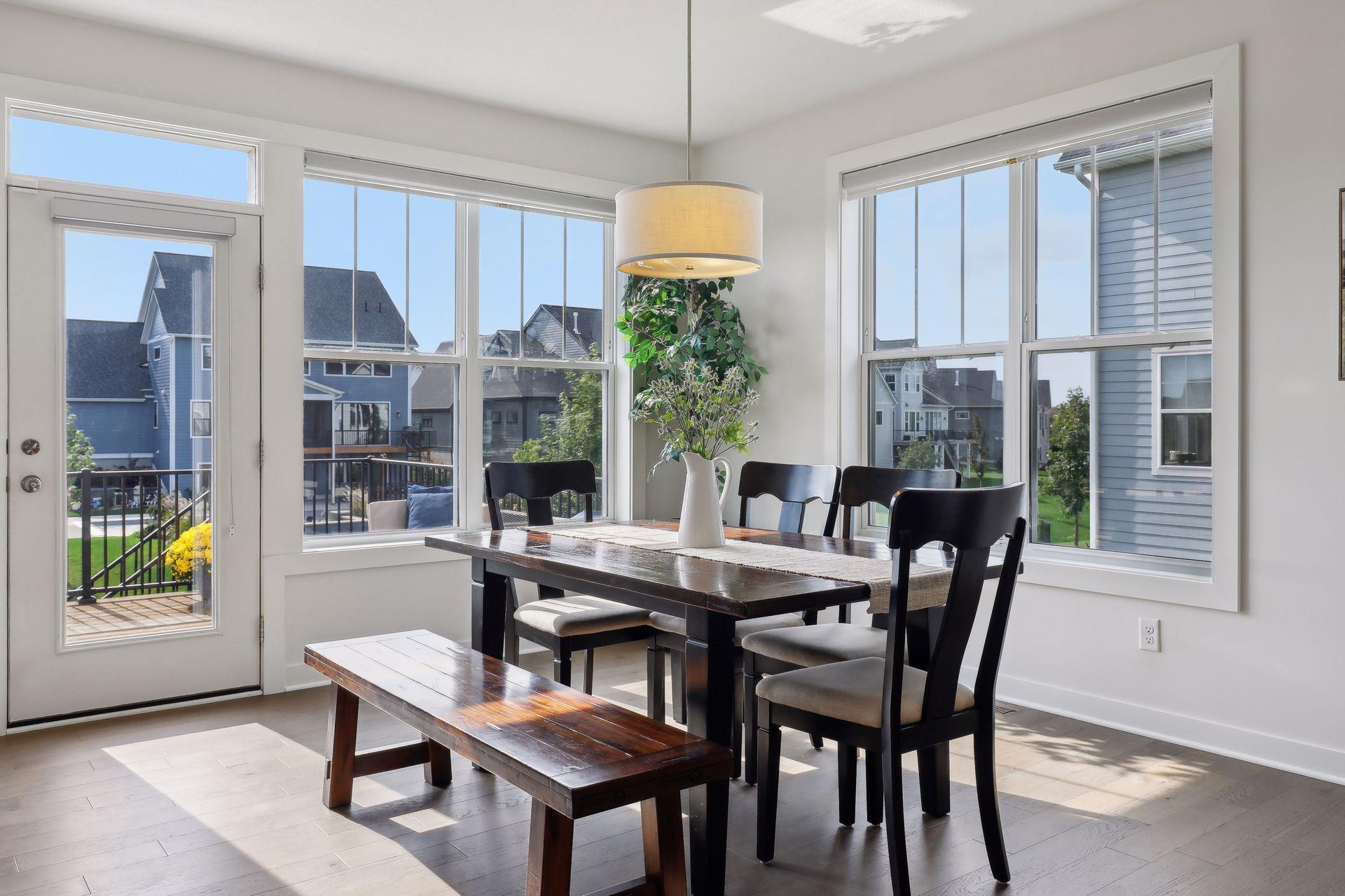 Bright dining room with a dark wood table and bench beside large windows and a glass door to the deck.