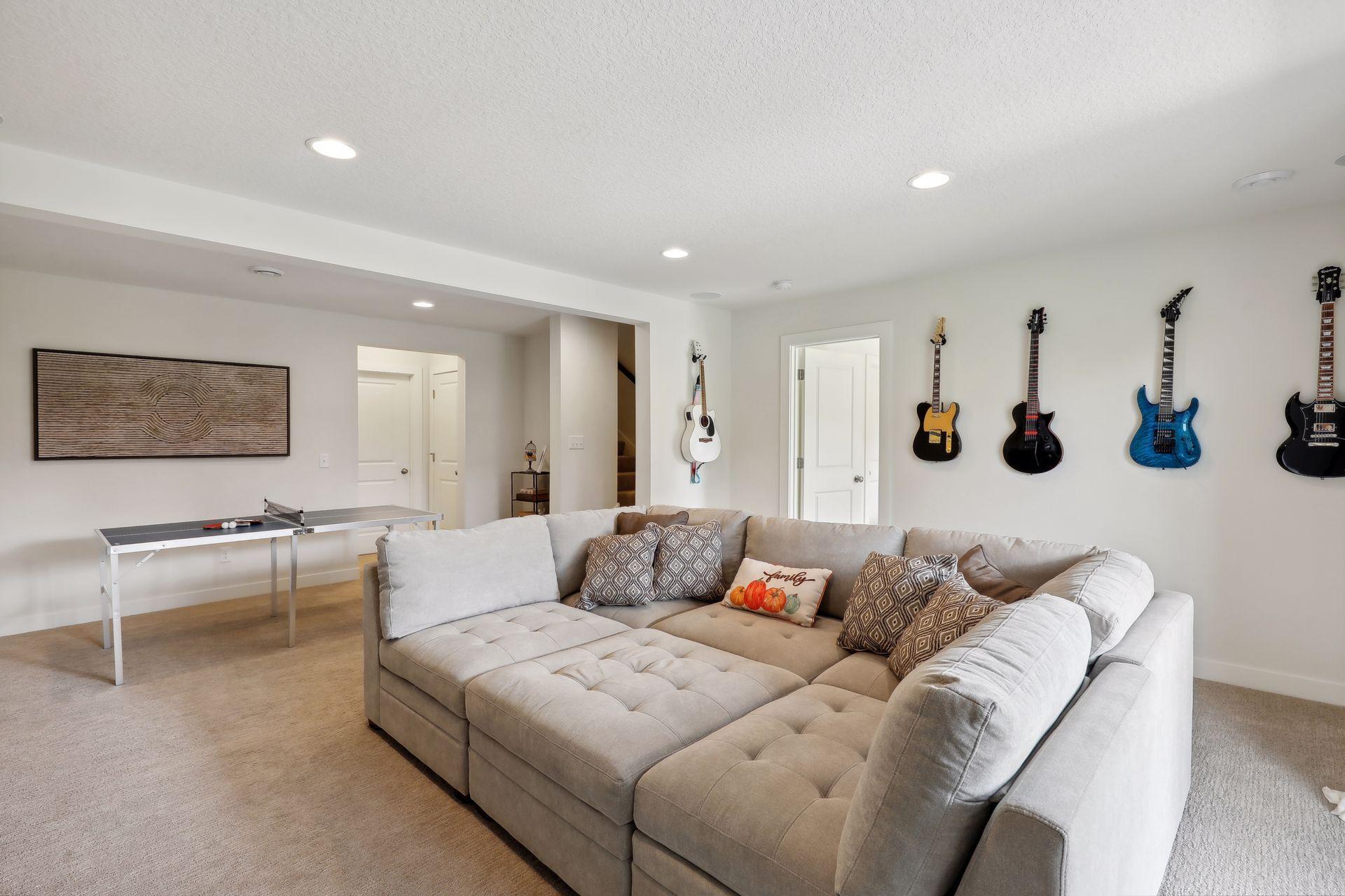 Furnished basement family room with a large sectional, wall-mounted guitars, and a table tennis table.