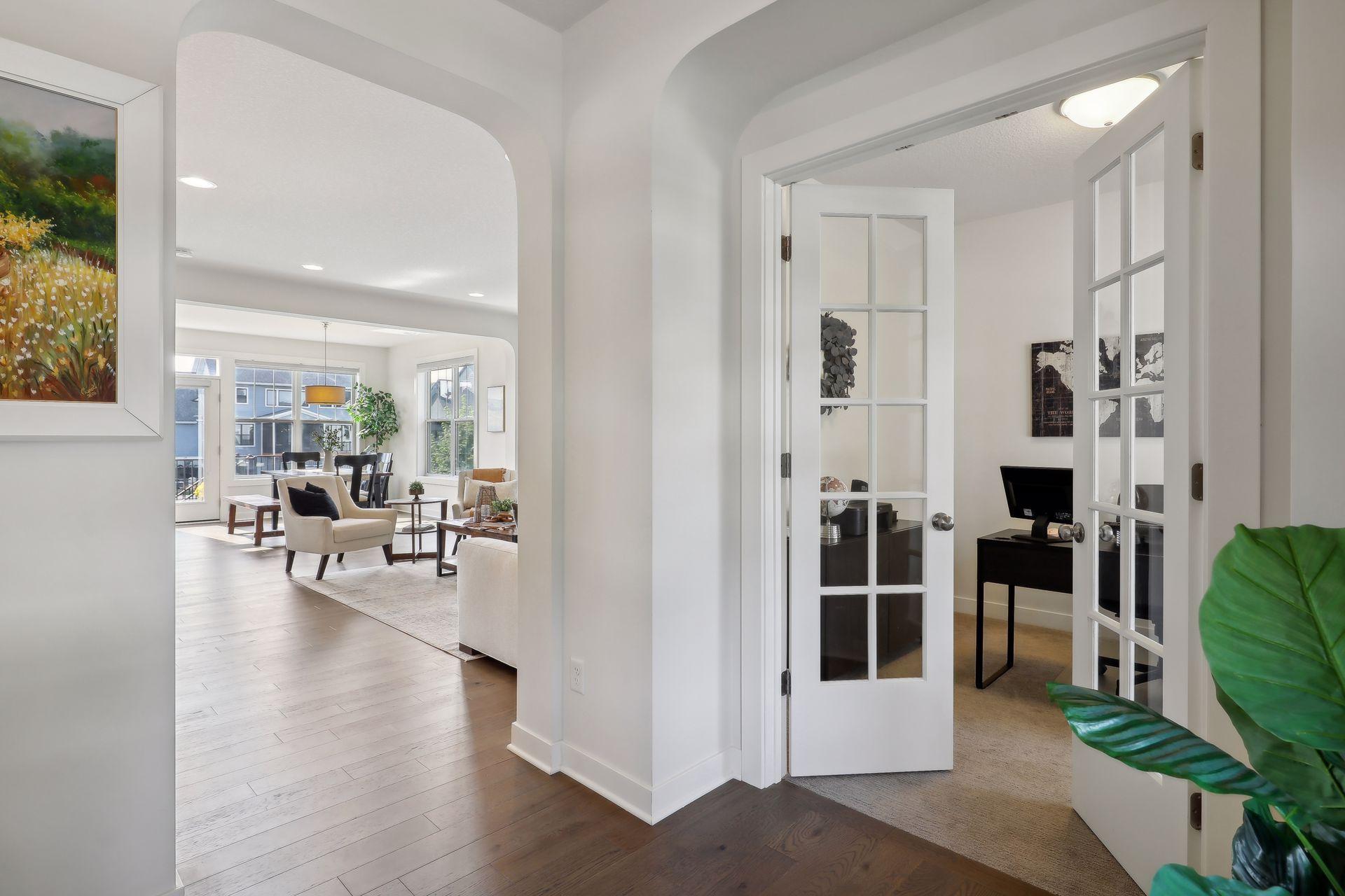 Bright home interior with an arched opening, living and dining area, and office behind French doors.