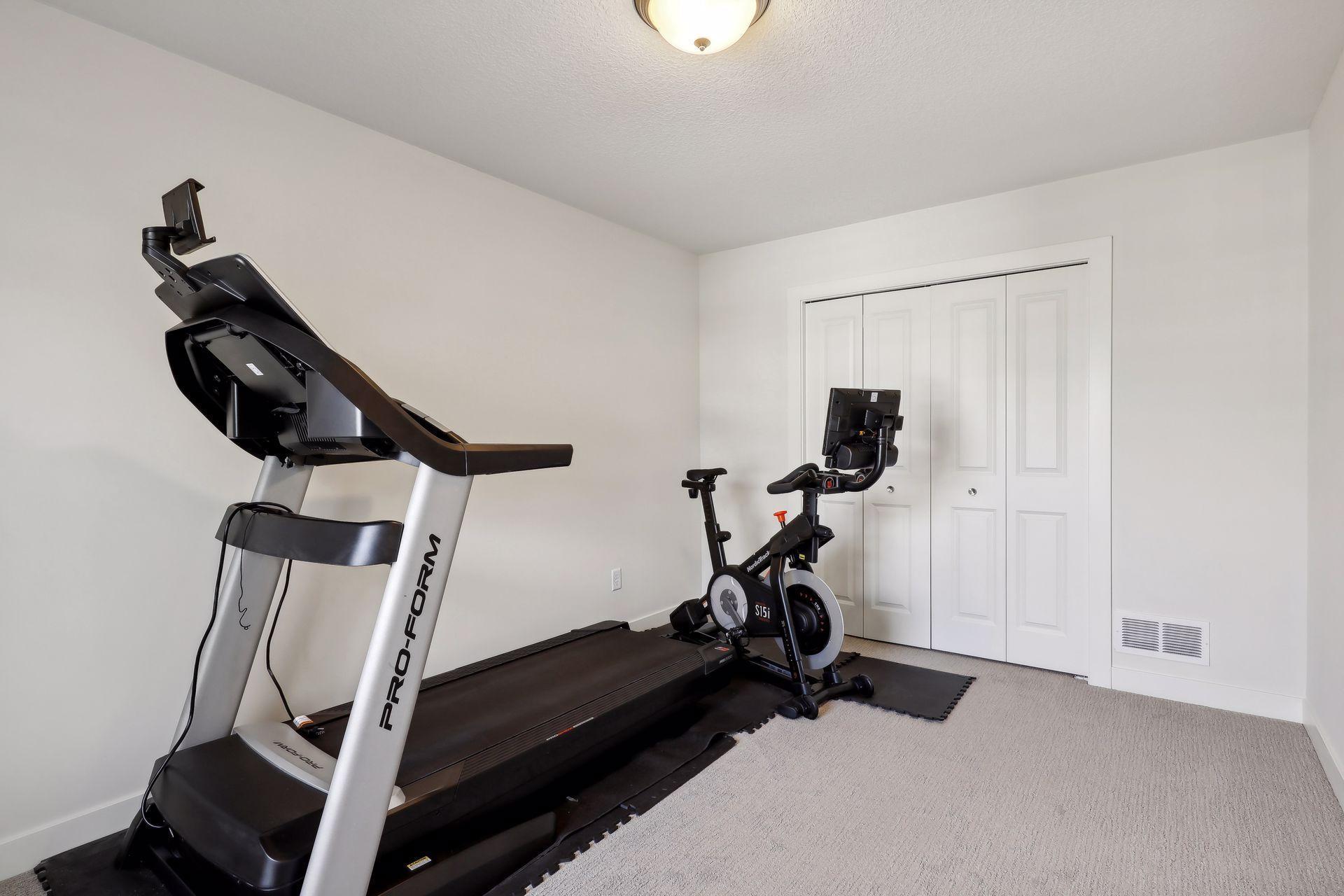Home gym with a treadmill and stationary bike on carpet beside white closet doors.