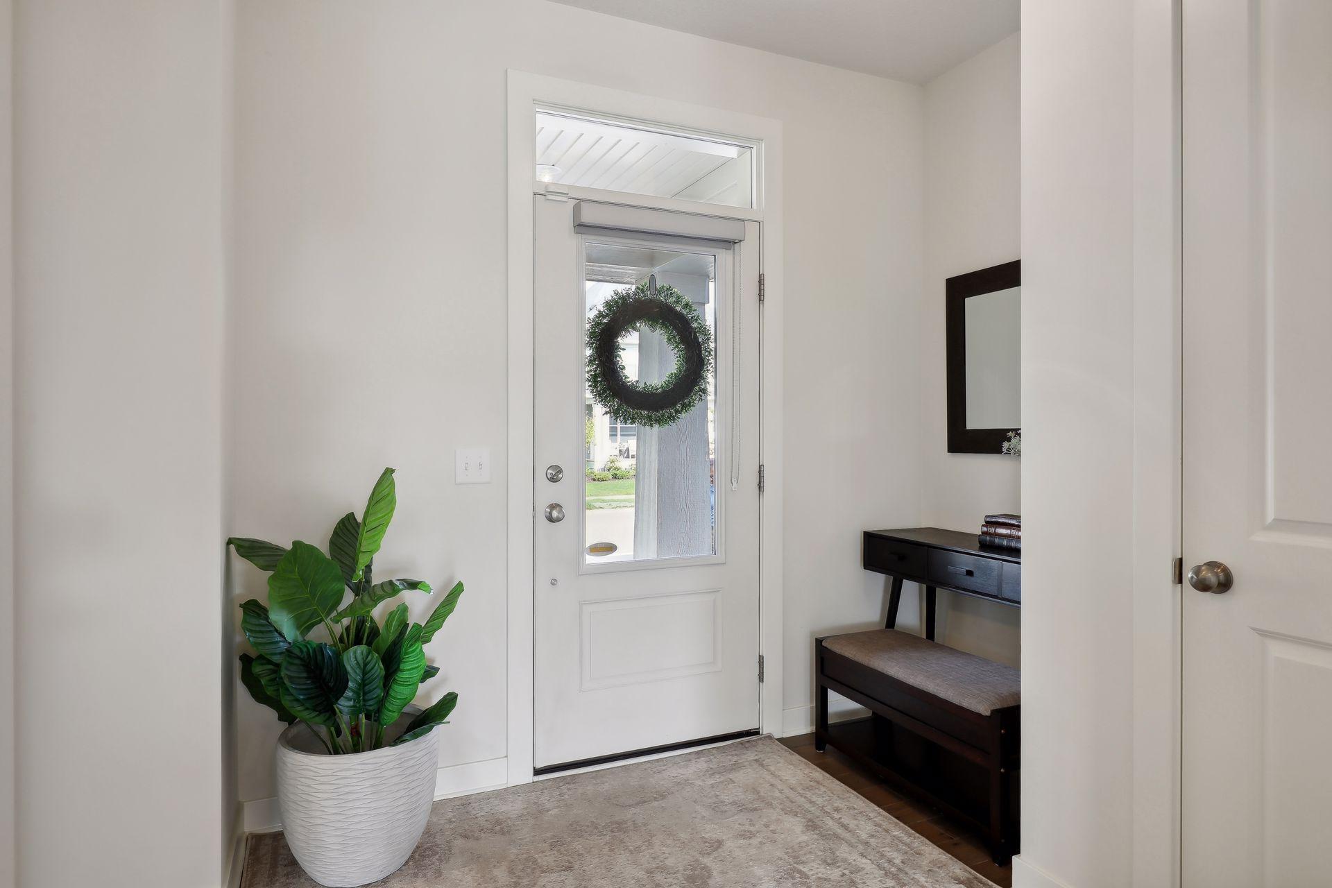 Bright entryway with a wreath on the glass-paneled front door, potted plant, and console bench.