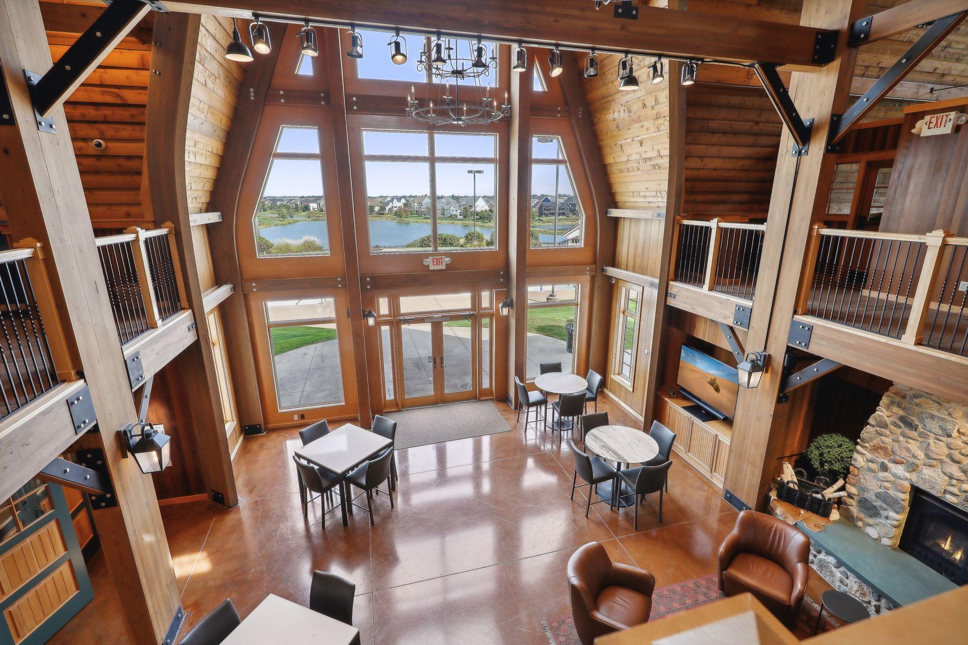 Lodge-style atrium with timber beams, lake-view windows, café tables, and a stone fireplace.