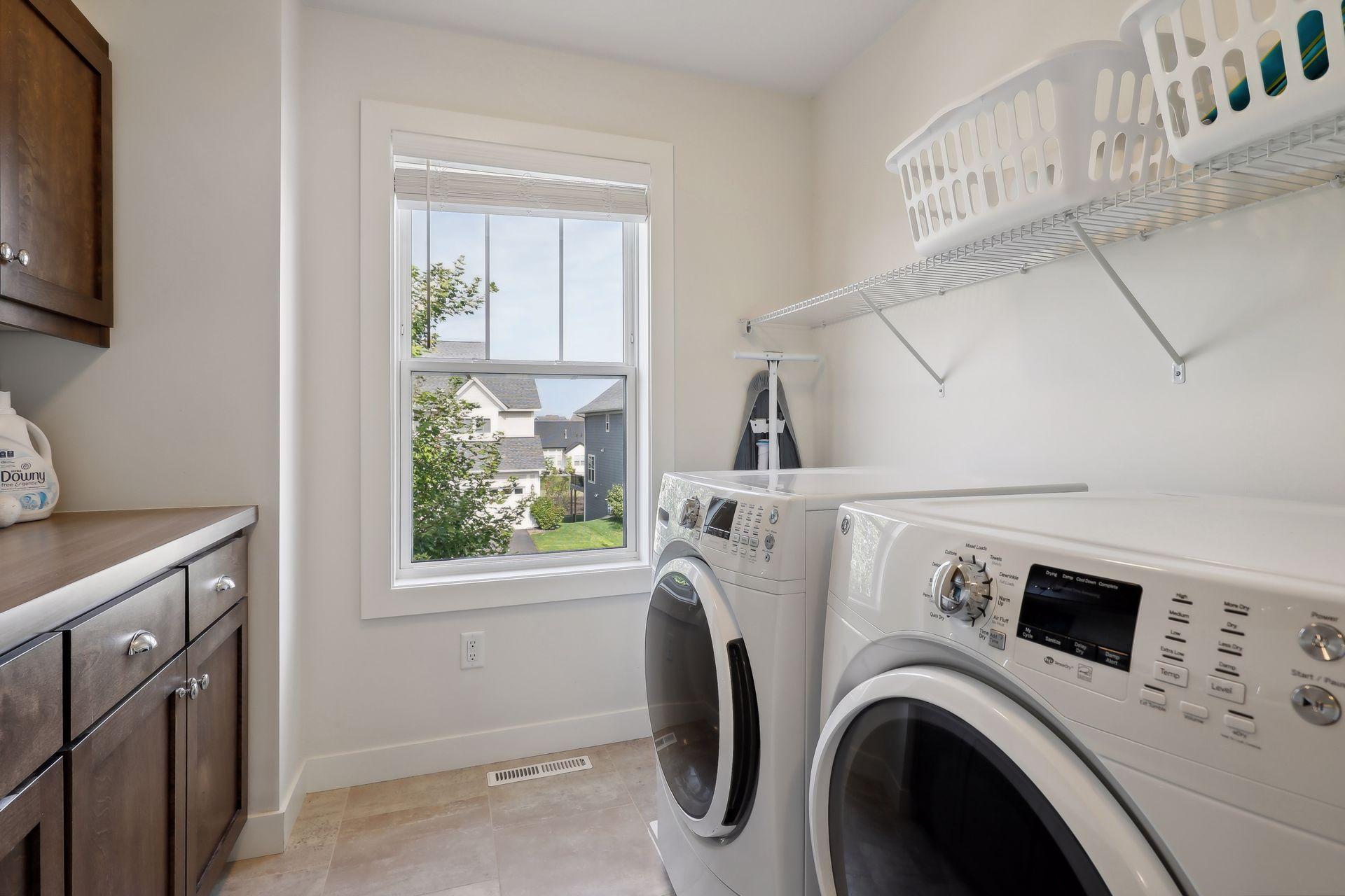 Laundry room with front-loading washer and dryer, dark wood cabinets, and a window overlooking neighboring homes.