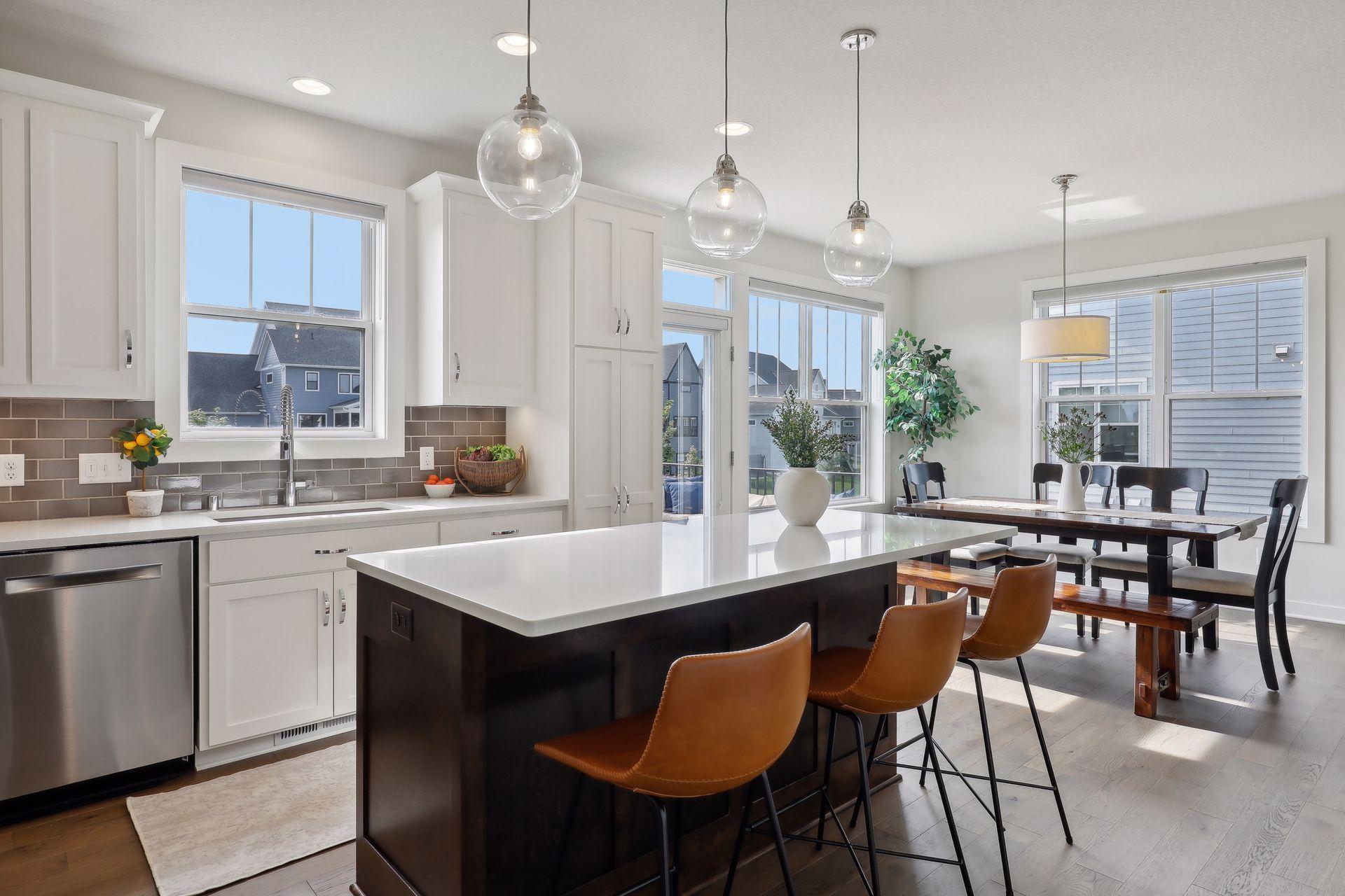 Kitchen and dining area with a large island, white cabinetry, and windows overlooking neighboring homes.