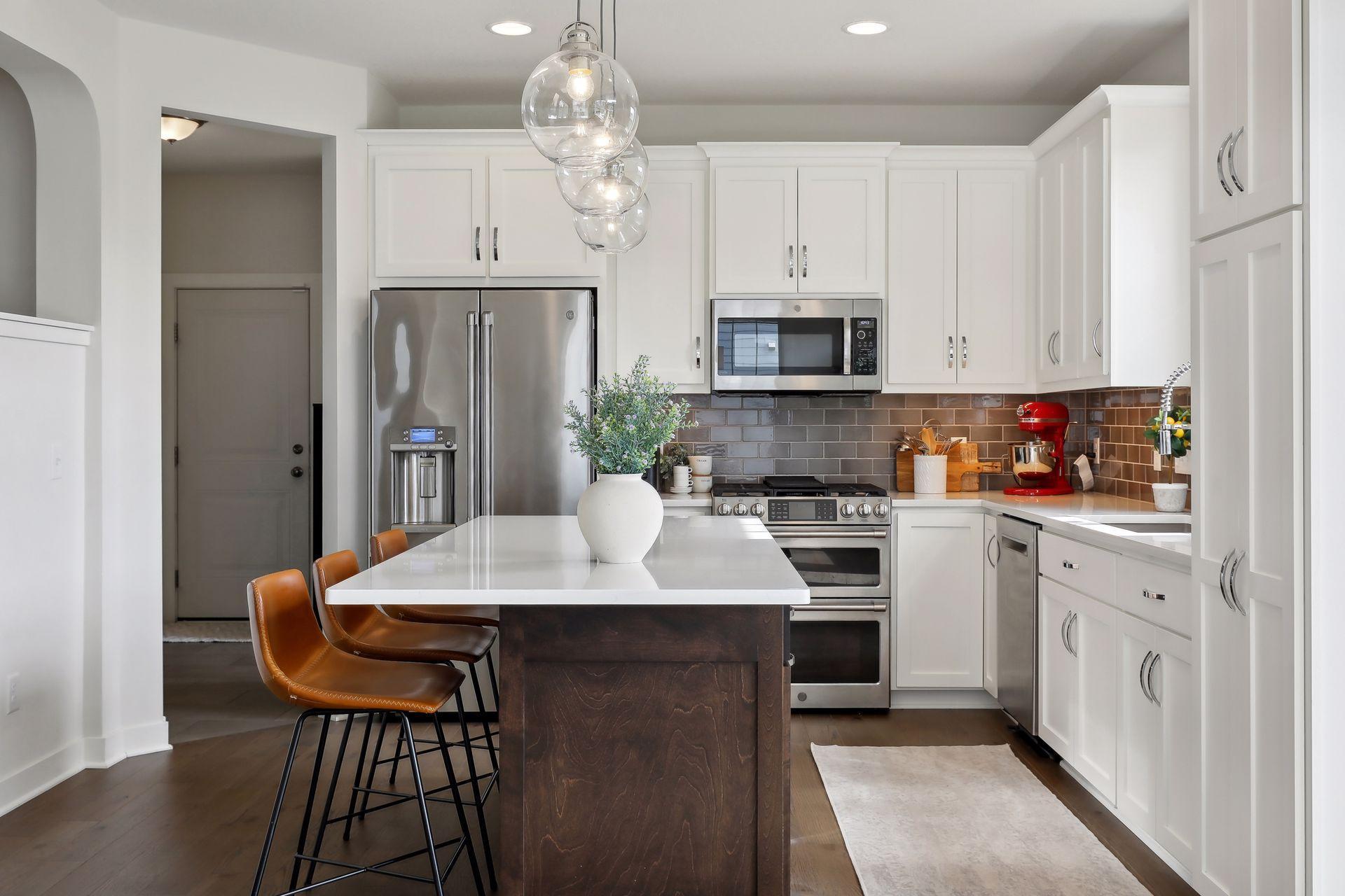 Kitchen with white cabinets, stainless appliances, a dark island, and gray tile backsplash.