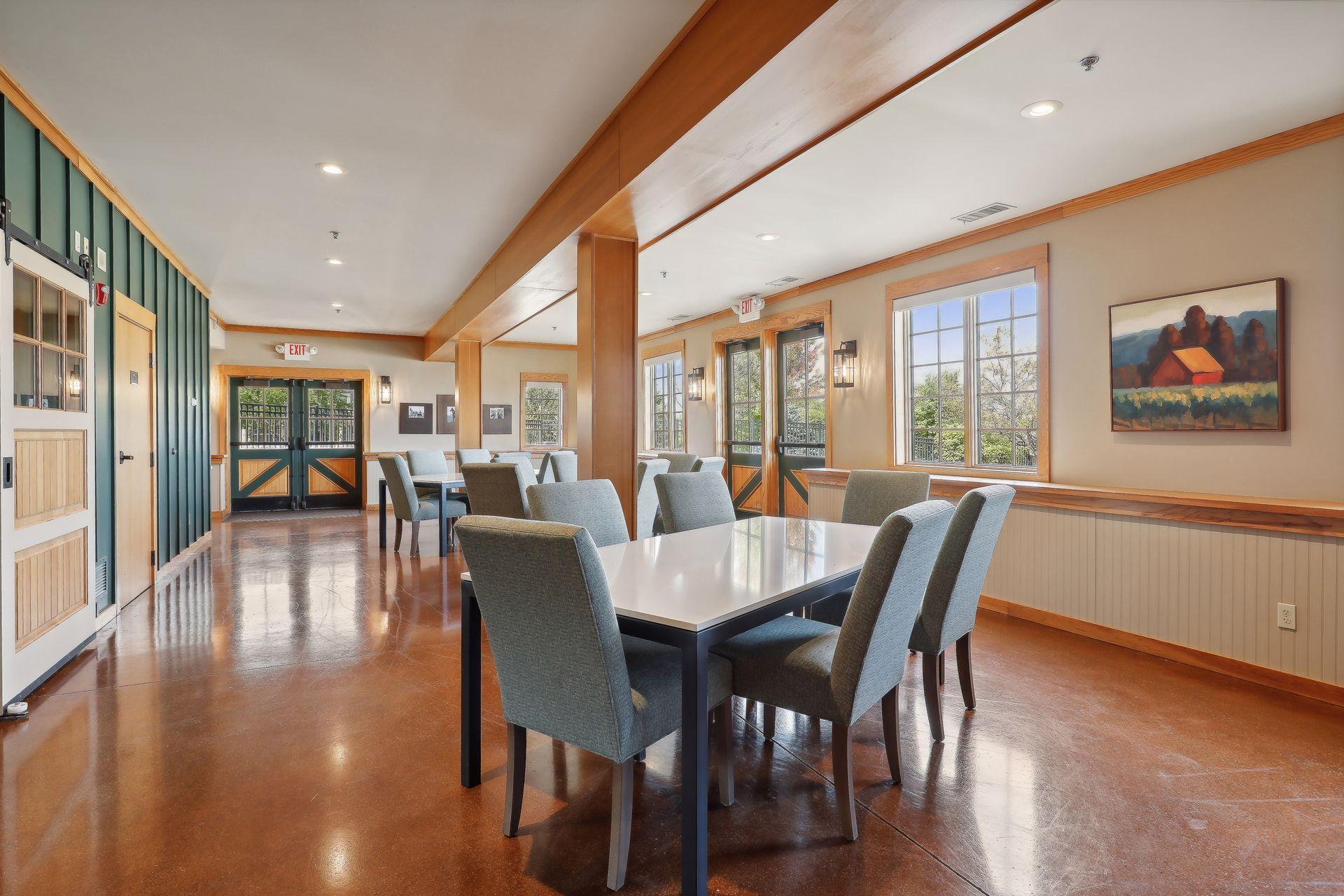Communal dining room with gray chairs, large windows, green paneling, and warm wood trim.