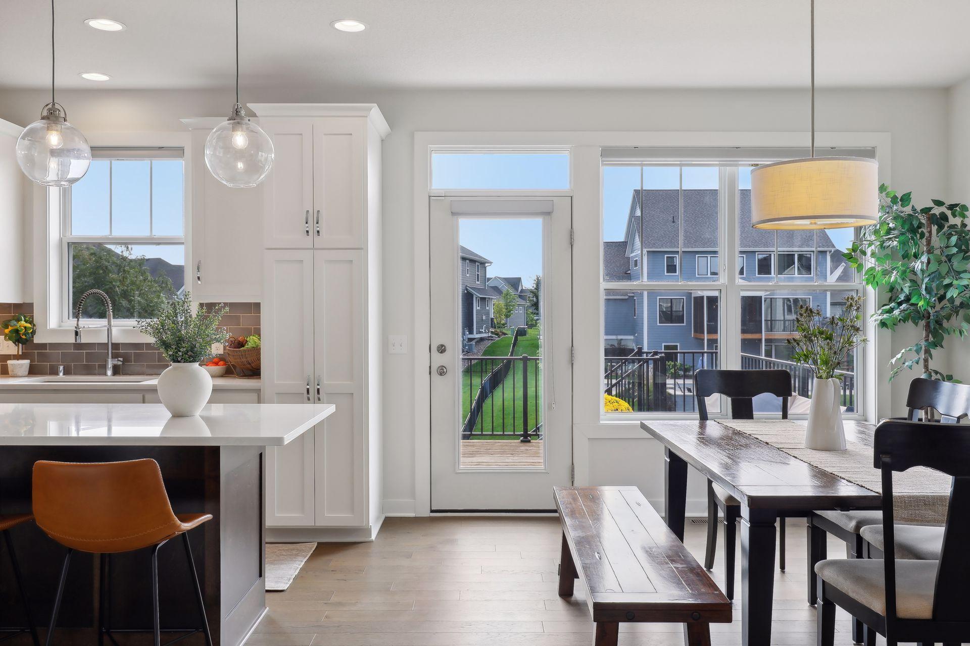 Open-plan kitchen and dining area with white island, wood table, and windows overlooking neighboring homes.