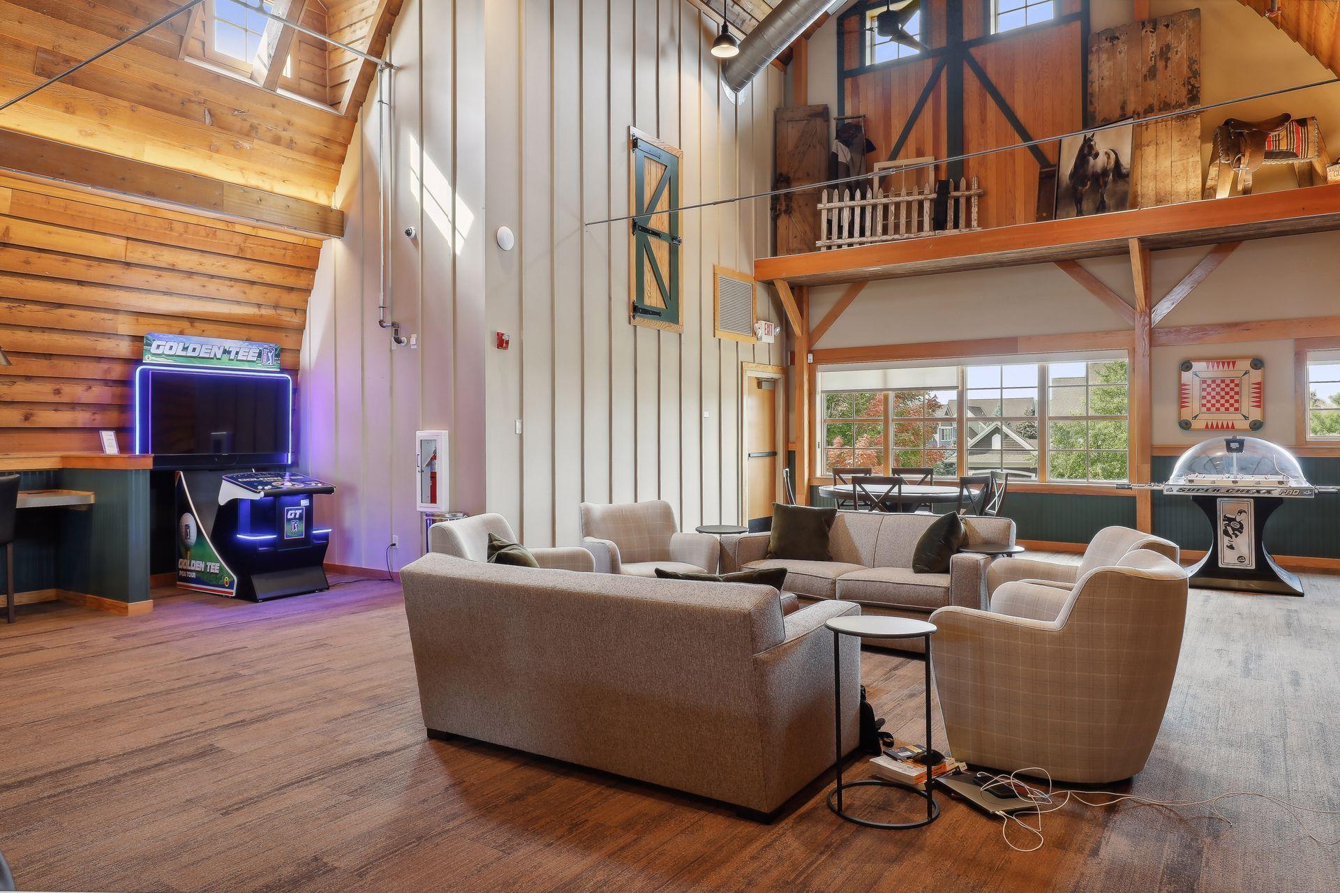 Double-height recreation room with timber beams, lounge seating, a Golden Tee game, and a loft.