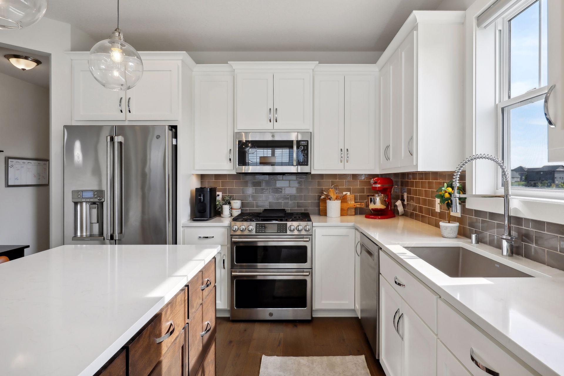 Modern white kitchen with stainless steel appliances, a large island, and a sink beneath a sunny window.