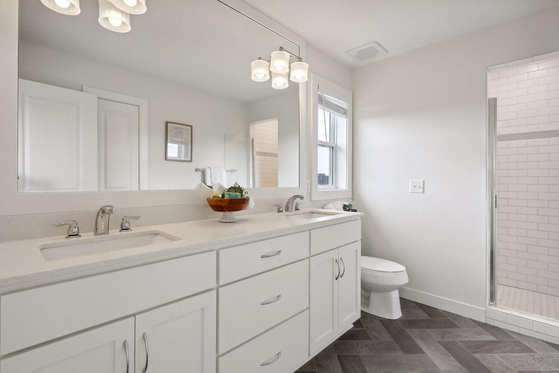 Bright bathroom with a white double vanity, large mirror, and glass-enclosed subway-tile shower.