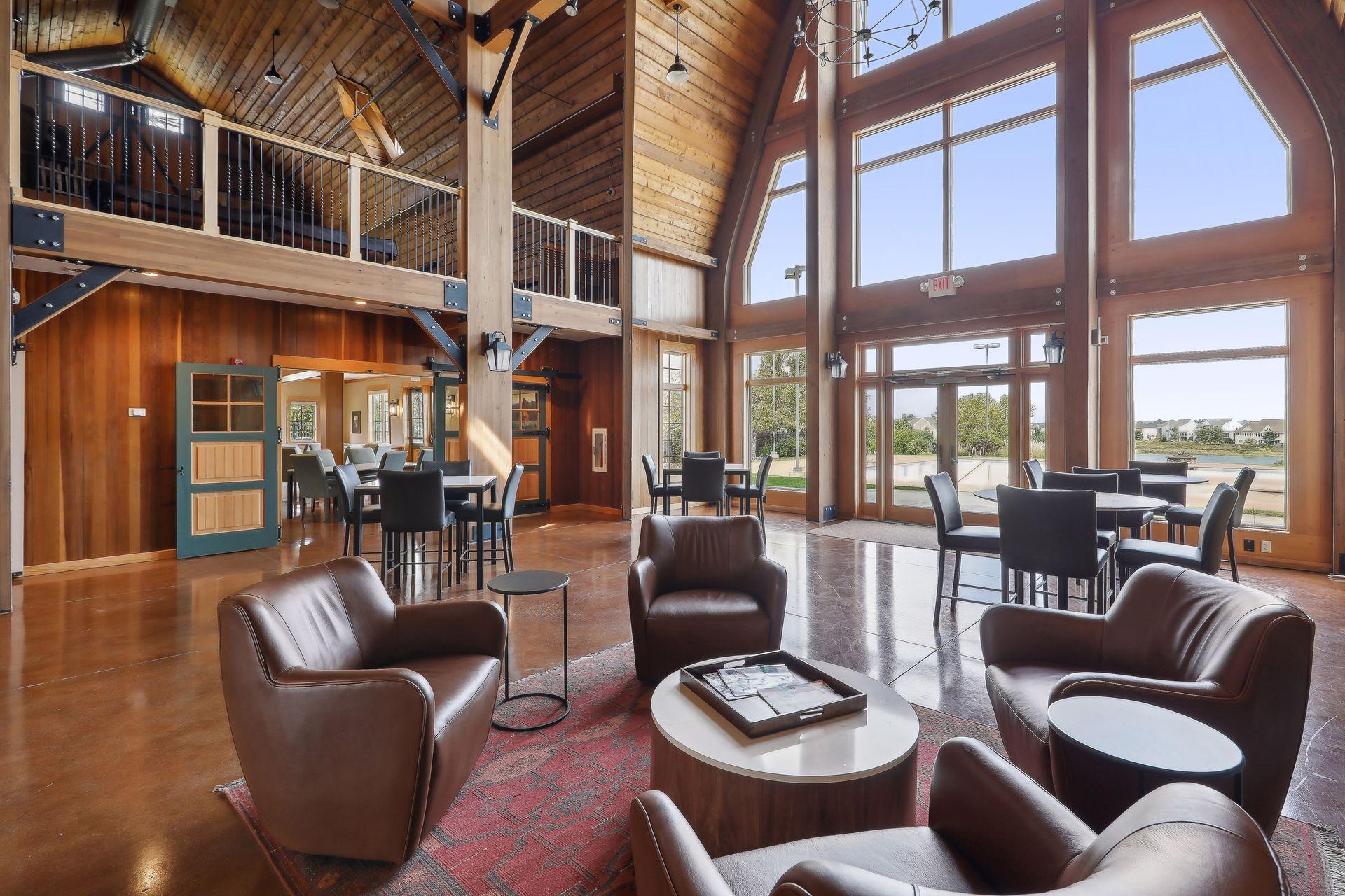 Lodge-style great room with exposed timber beams, leather chairs, and tall windows overlooking a pool and water.