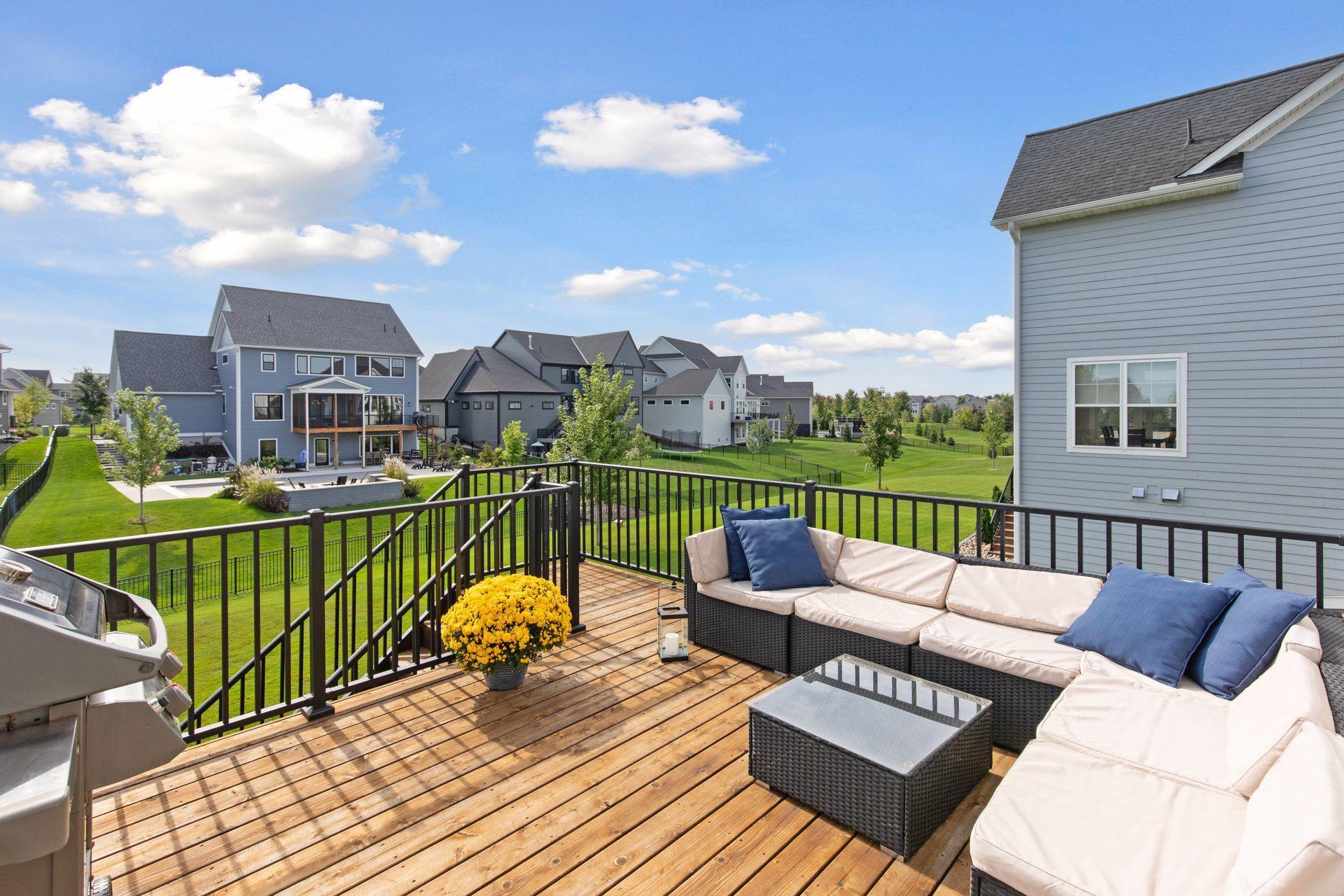Furnished wooden deck with sectional seating overlooks green lawns and neighboring homes.