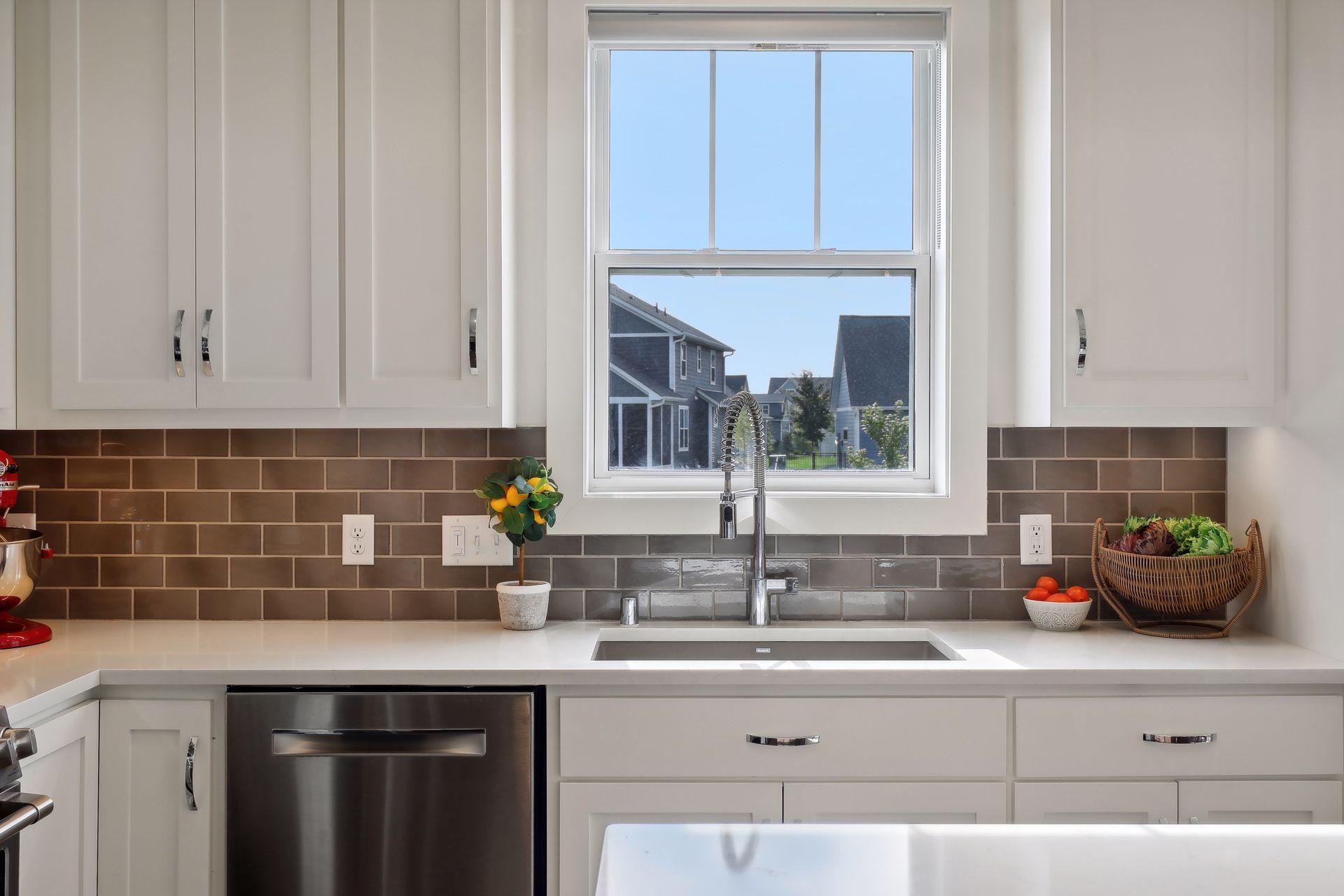 Kitchen with white cabinets, subway tile backsplash, and a sink beneath a large window.