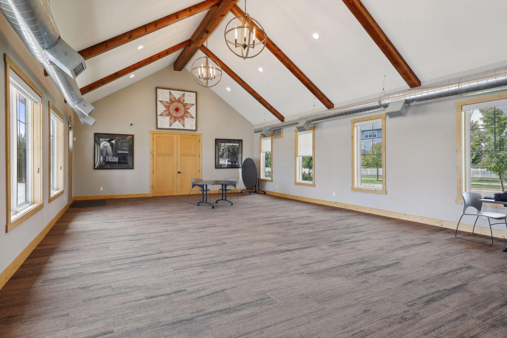 Spacious vaulted room with exposed wood beams, large windows, and a small table and chairs.