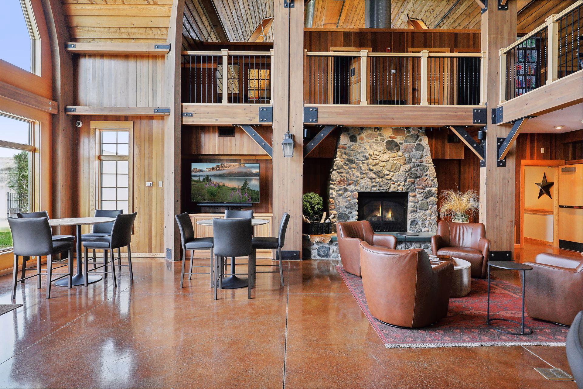 Furnished great room with a soaring timber ceiling, open balcony, and large stone fireplace.