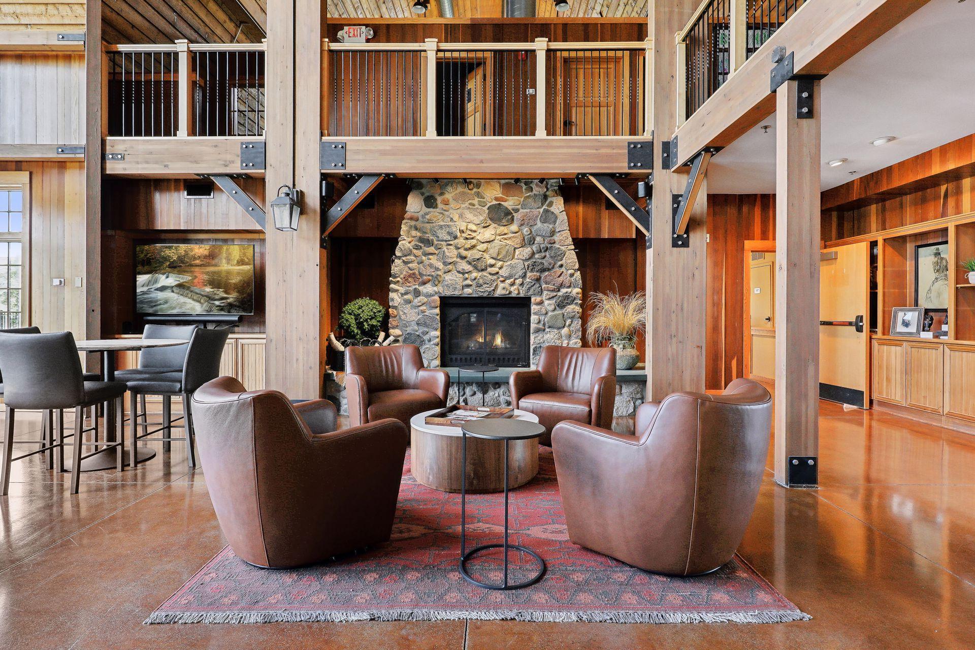 Double-height living room with a stone fireplace, exposed timber beams, and leather armchairs.