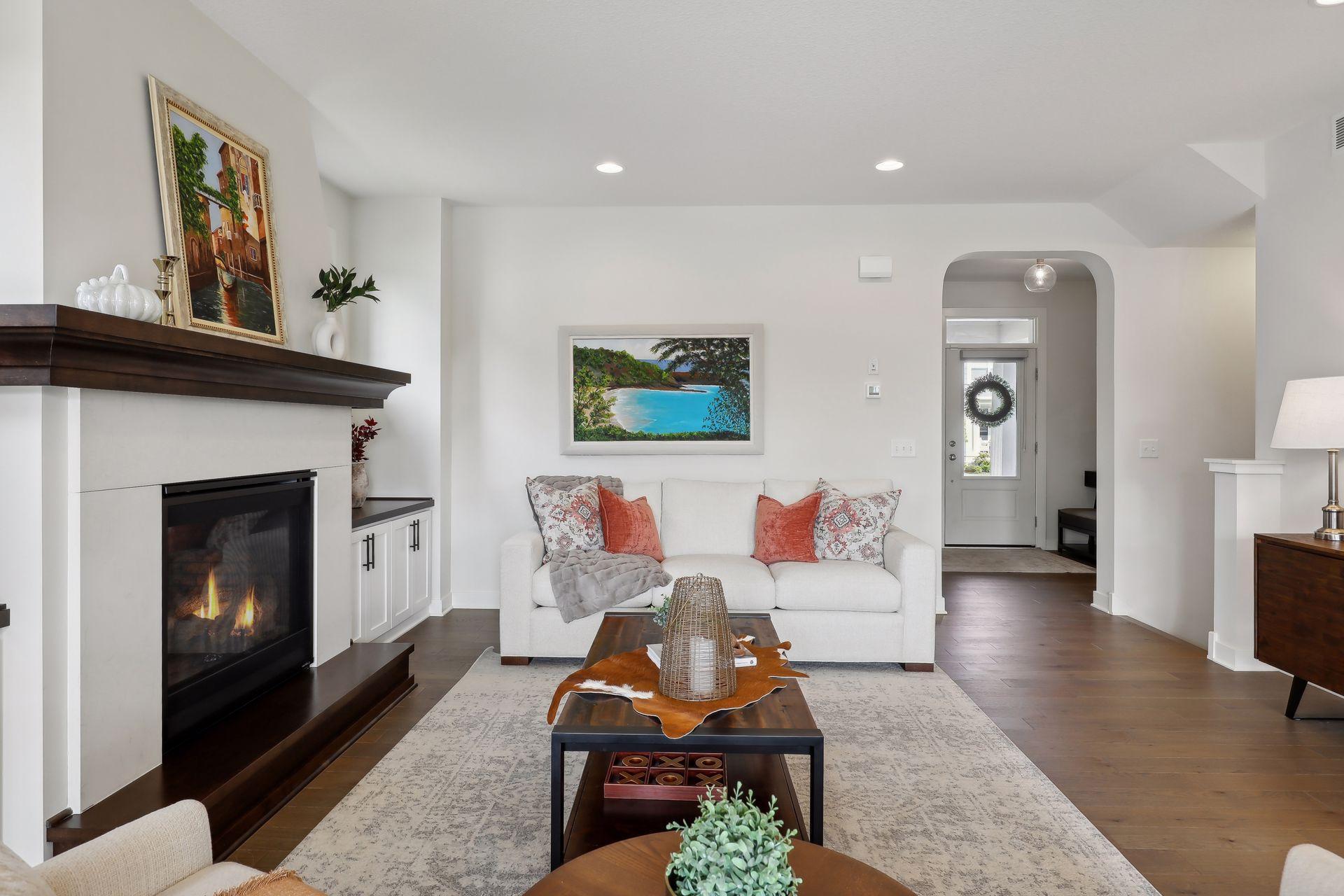 Staged living room with a white sofa, dark wood coffee table, and lit fireplace.