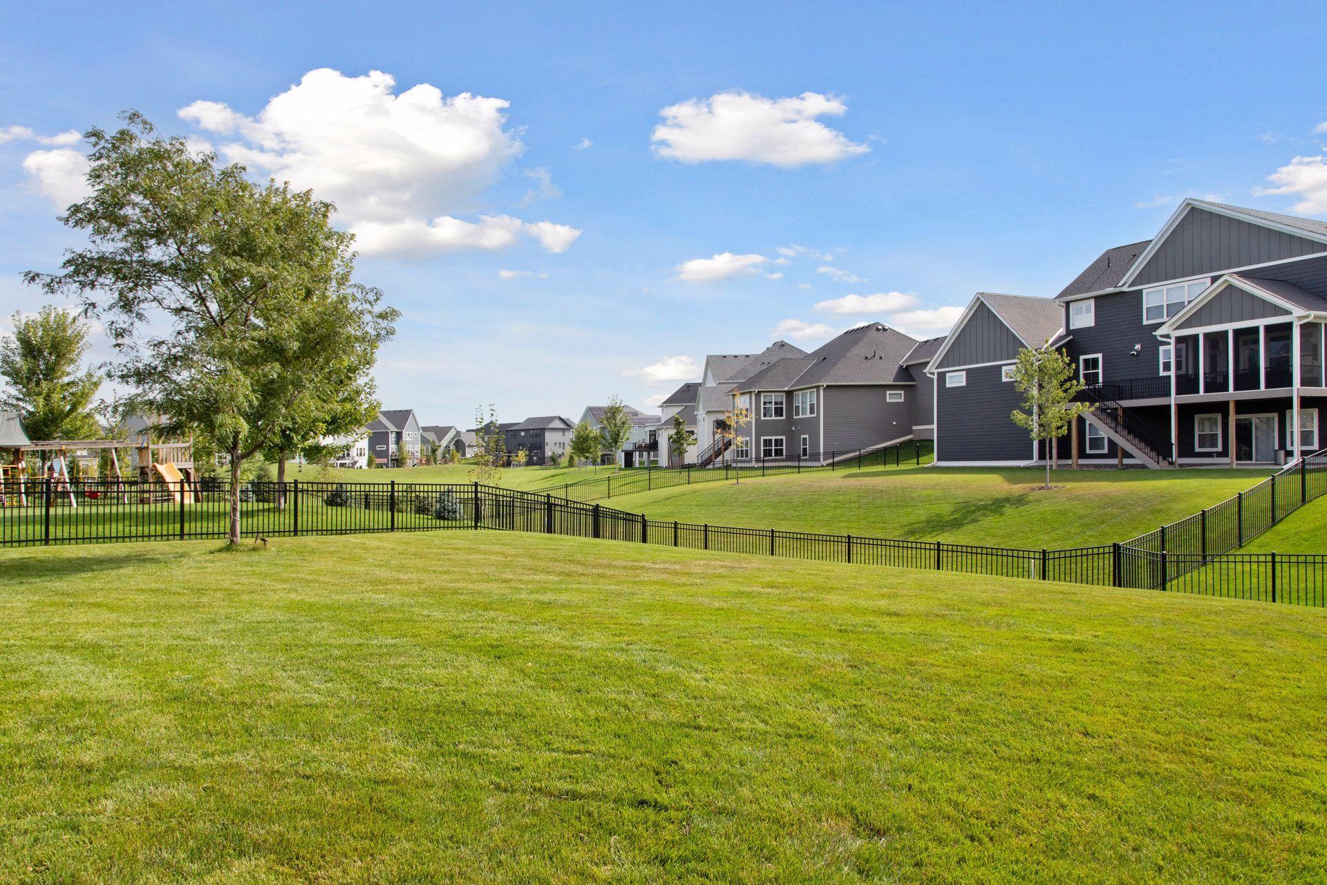 Grassy neighborhood common area with fenced backyards, modern homes, and a playground.