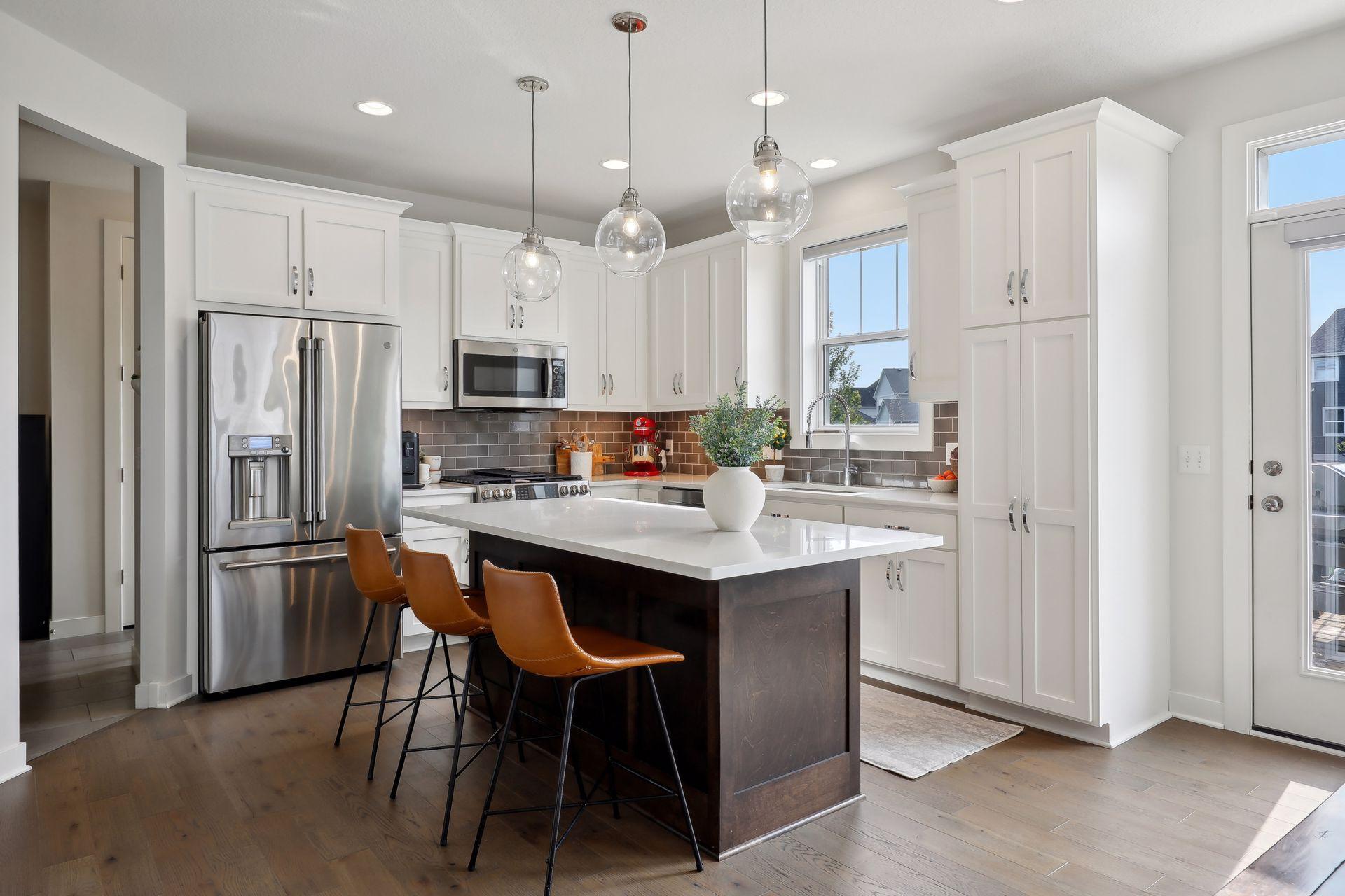 Bright kitchen with a dark island, white cabinets, stainless appliances, and brown bar stools.