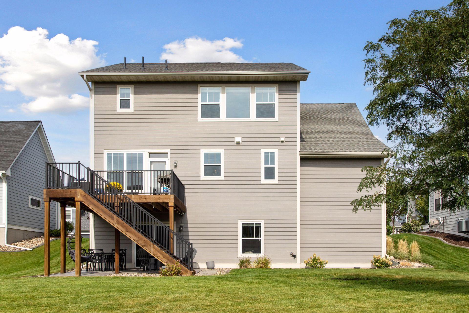 Rear of the gray two-story home with a raised deck, wooden stairs, and broad green lawn.