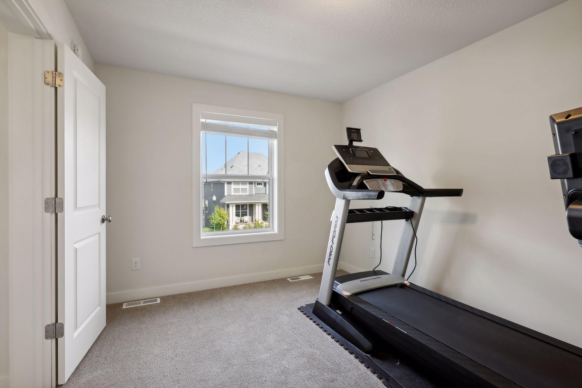 Home exercise room with a treadmill beside a window overlooking a neighboring house.