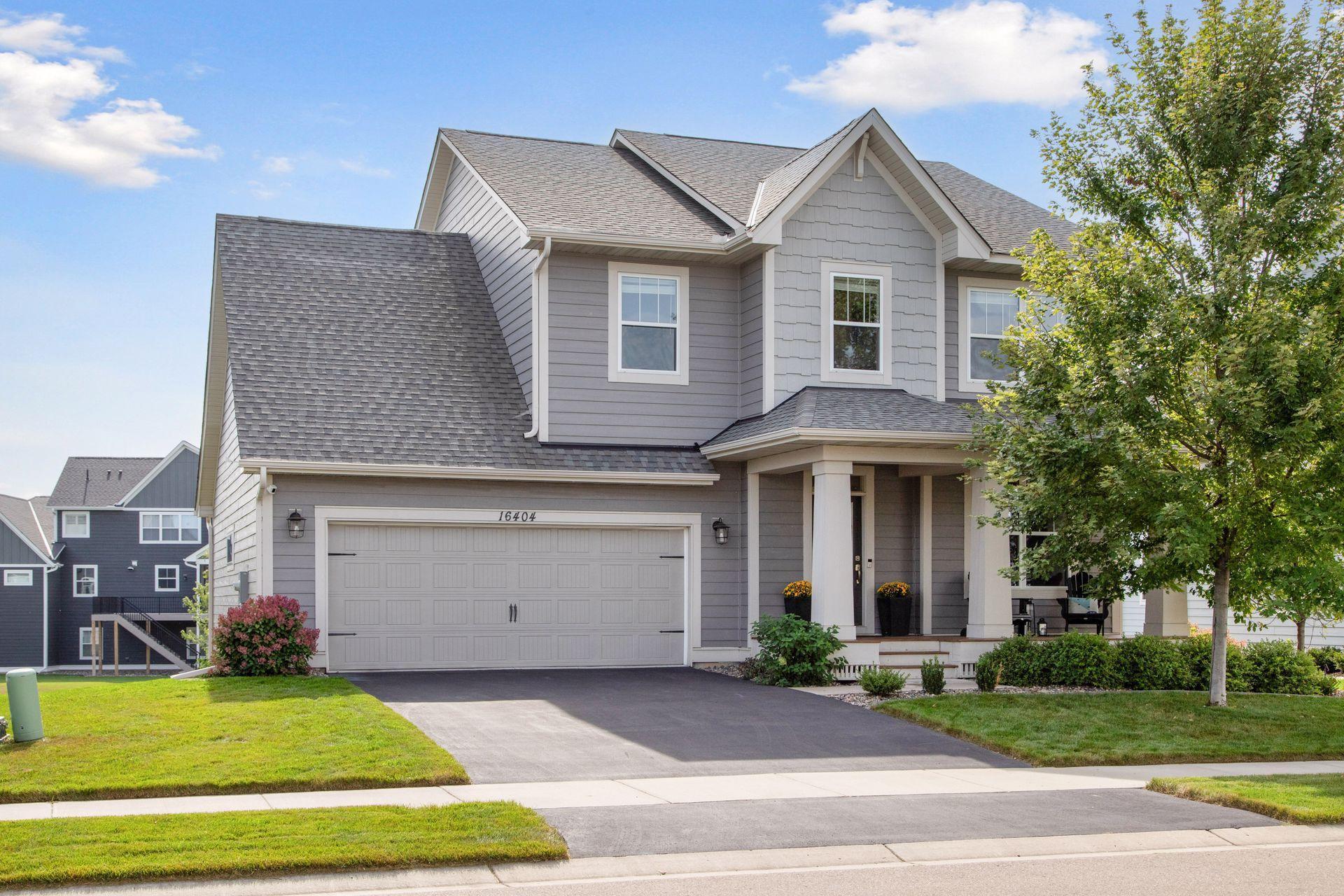 Gray two-story home with a double garage, covered porch, and mature tree beside the driveway.