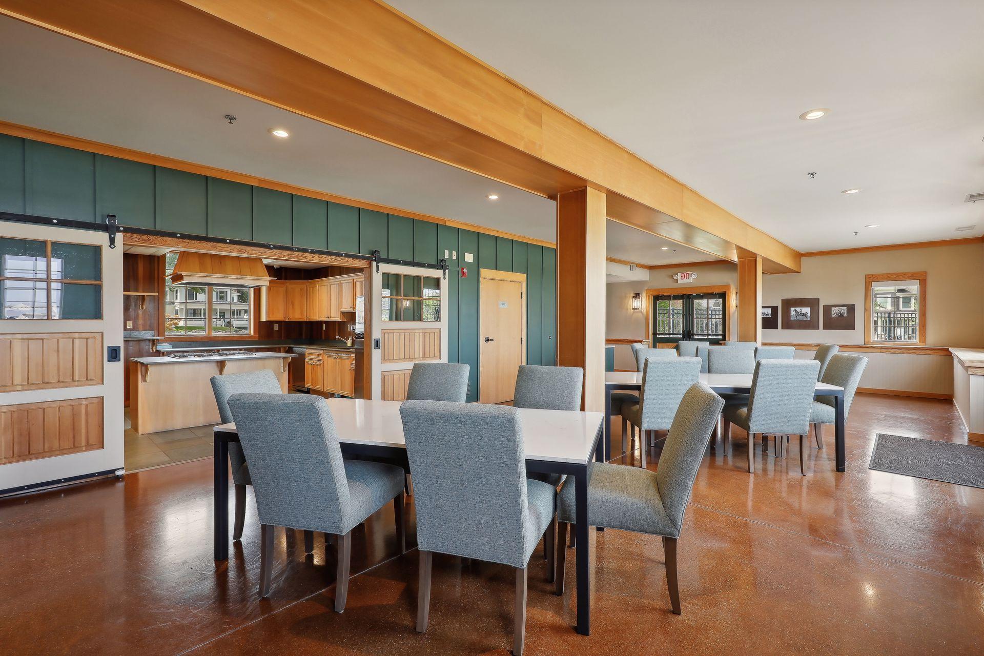 Dining area with gray chairs, multiple tables, and an adjoining wood-cabinet kitchen.