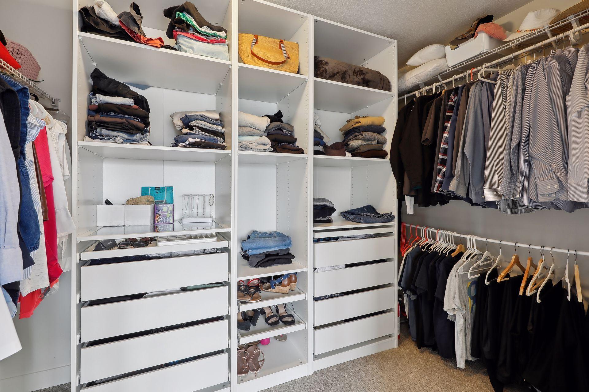 Walk-in closet with built-in white shelving, drawers, and hanging clothes.