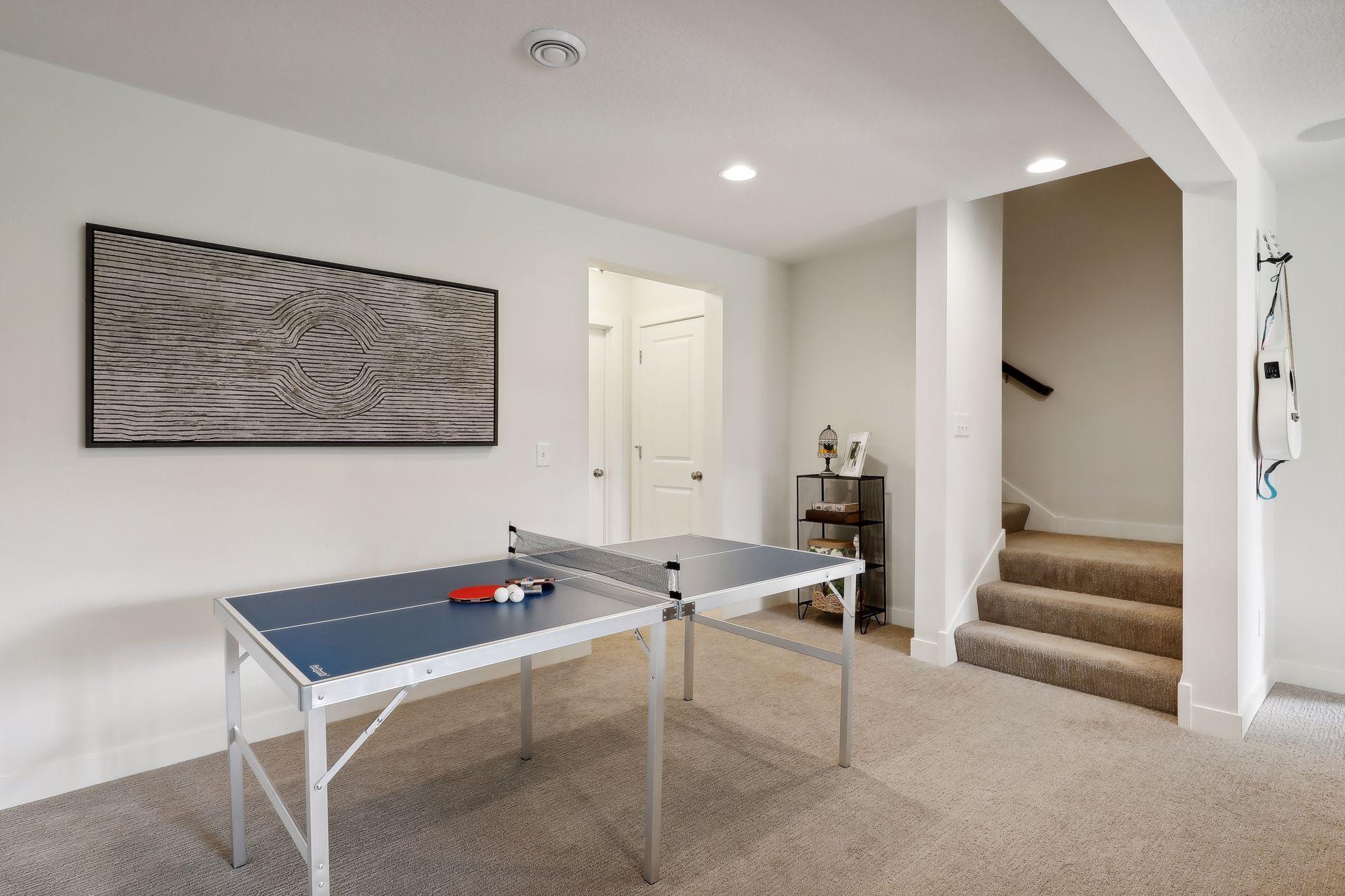 Recreation room with a ping-pong table, framed wall art, and carpeted stairs.