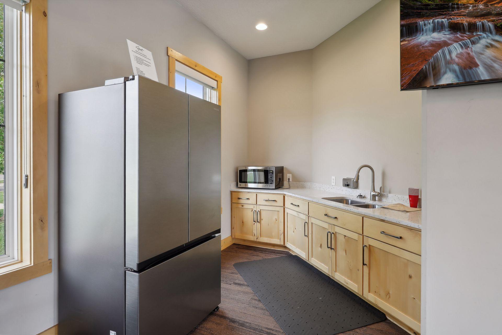 Kitchen with light wood cabinets, a large stainless steel refrigerator, and a double-basin sink.
