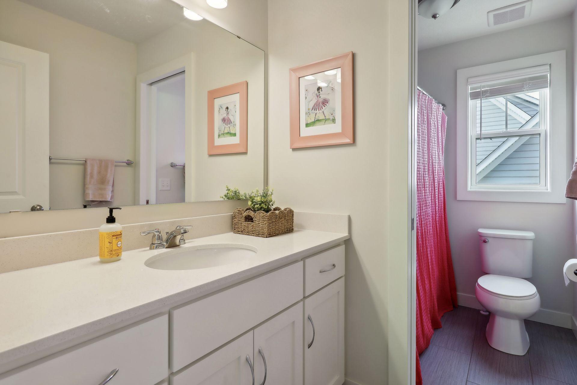 Bathroom with a white vanity and large mirror beside a toilet and pink shower curtain.