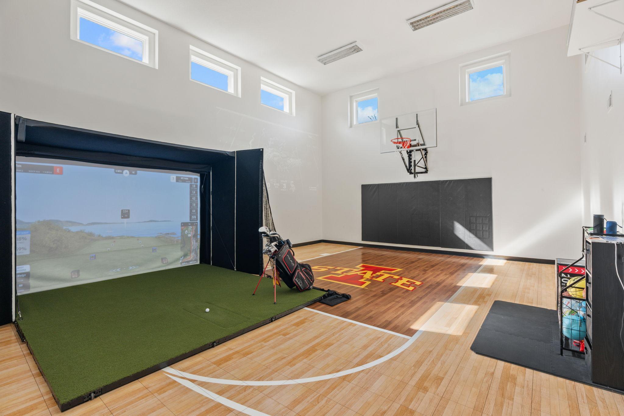 Indoor sports room with a basketball court and golf simulator hitting bay.