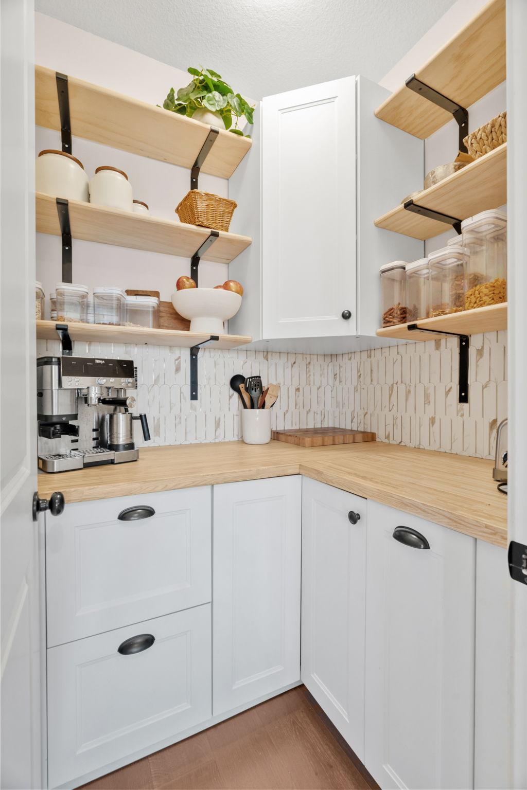 Compact kitchen pantry with open wood shelves, white cabinets, butcher-block counters, and a coffee machine.