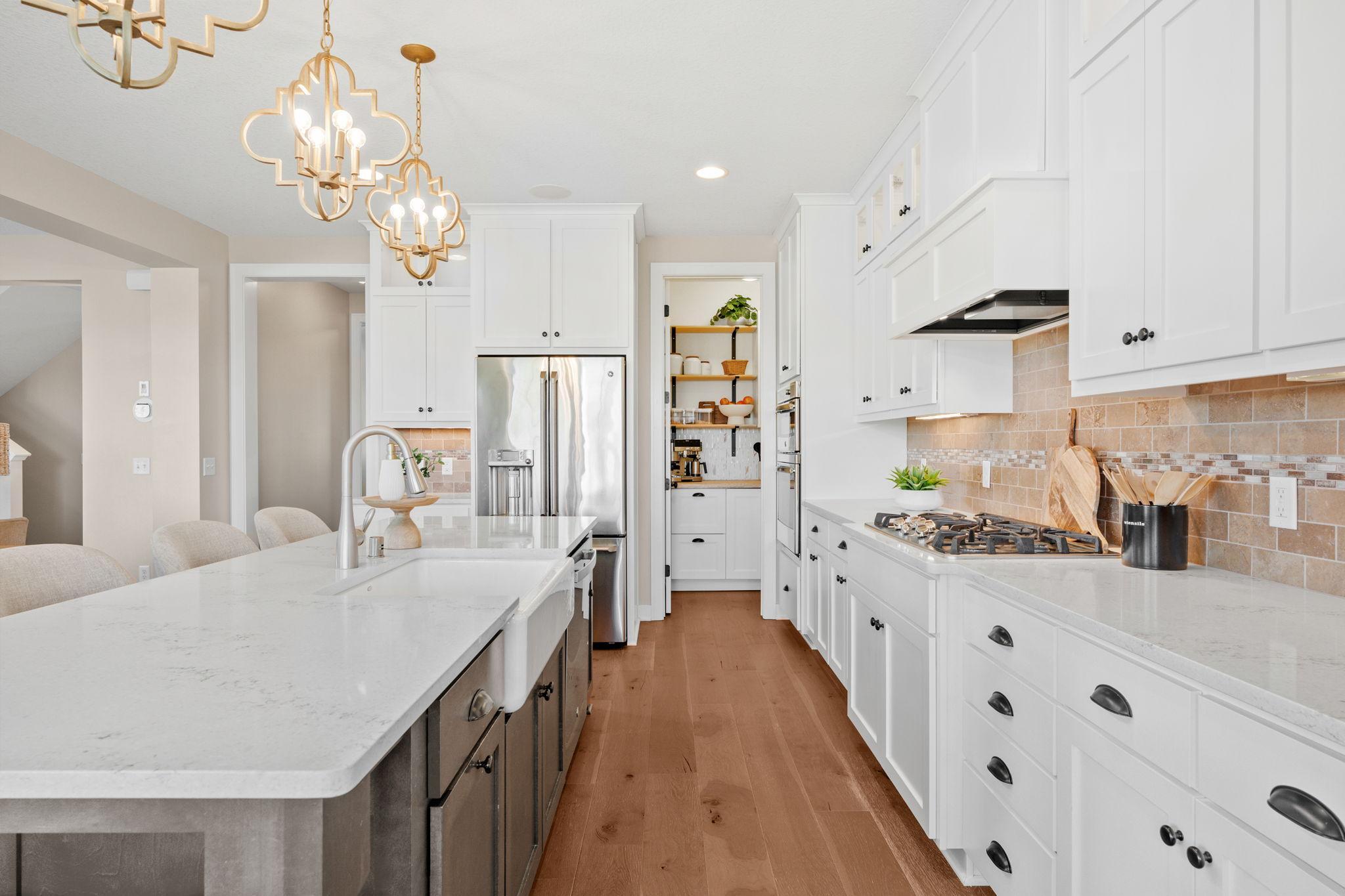 Bright kitchen with a quartz island, white cabinets, stainless appliances, and warm wood floors.