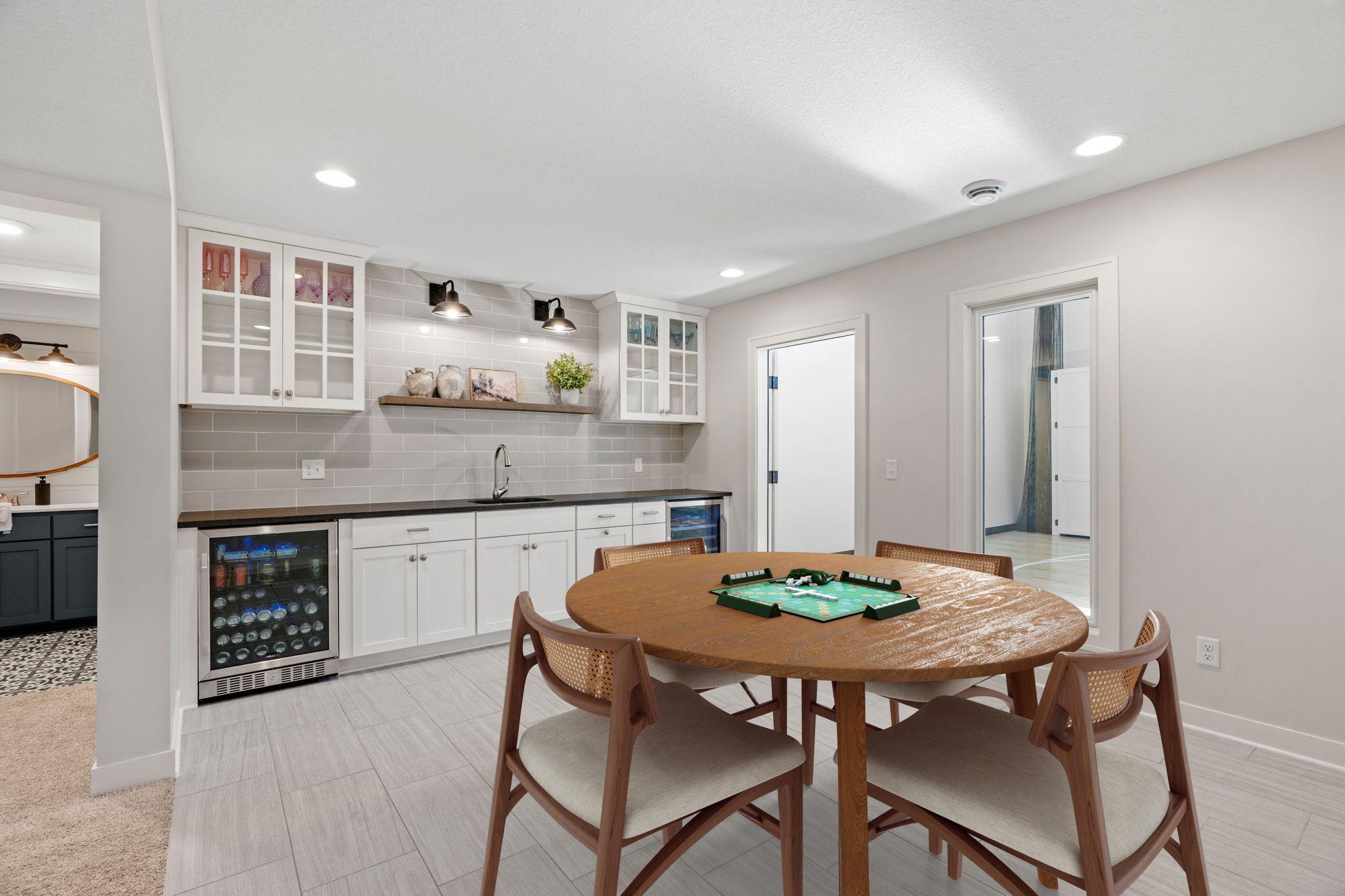 Dining and game area with a round wooden table beside a built-in wet bar and beverage refrigerators.
