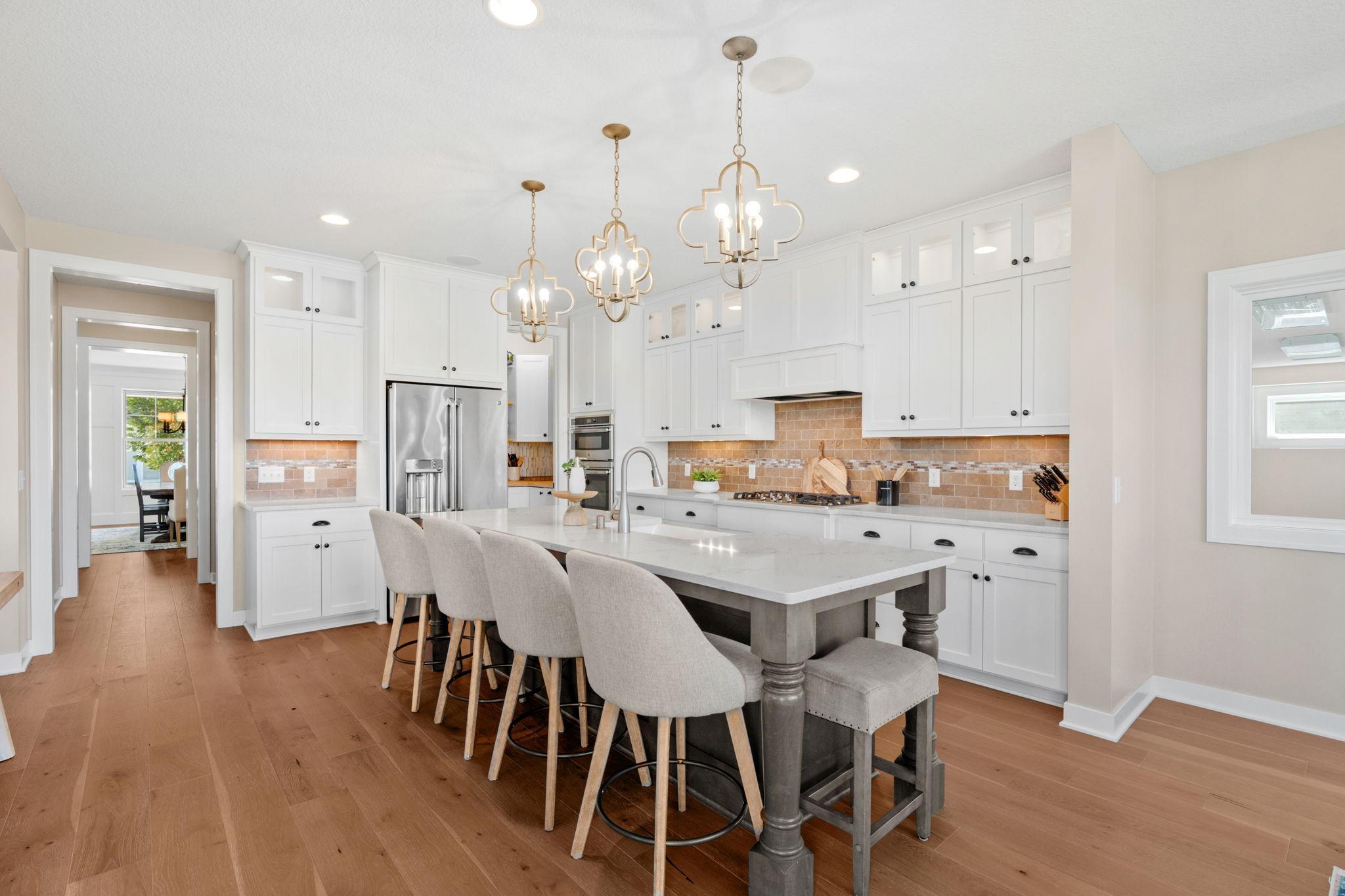 Bright kitchen with white cabinets, a large island with seating, stainless steel appliances, and brass pendant lights.