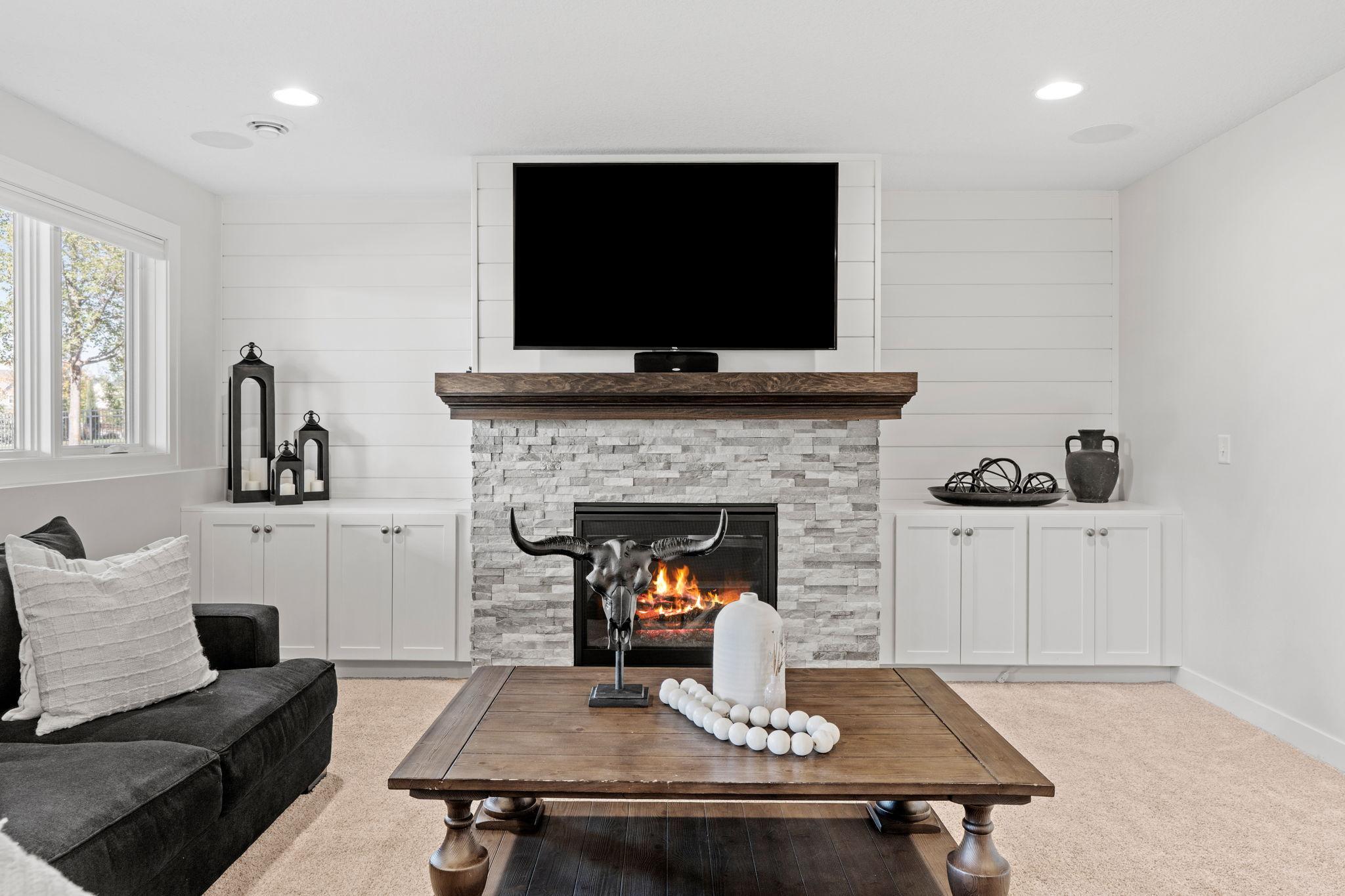 Living room with a stone fireplace, lit fire, built-in cabinets, and dark sectional sofa.