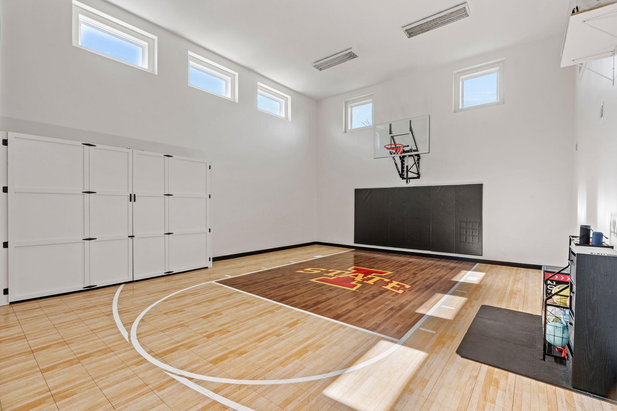 Indoor home basketball court with a polished wood floor, wall-mounted hoop, and red-and-gold center-court design.