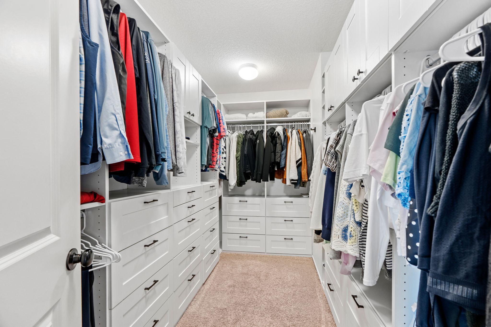 Walk-in closet with white built-in drawers, extensive hanging space, and beige carpet.
