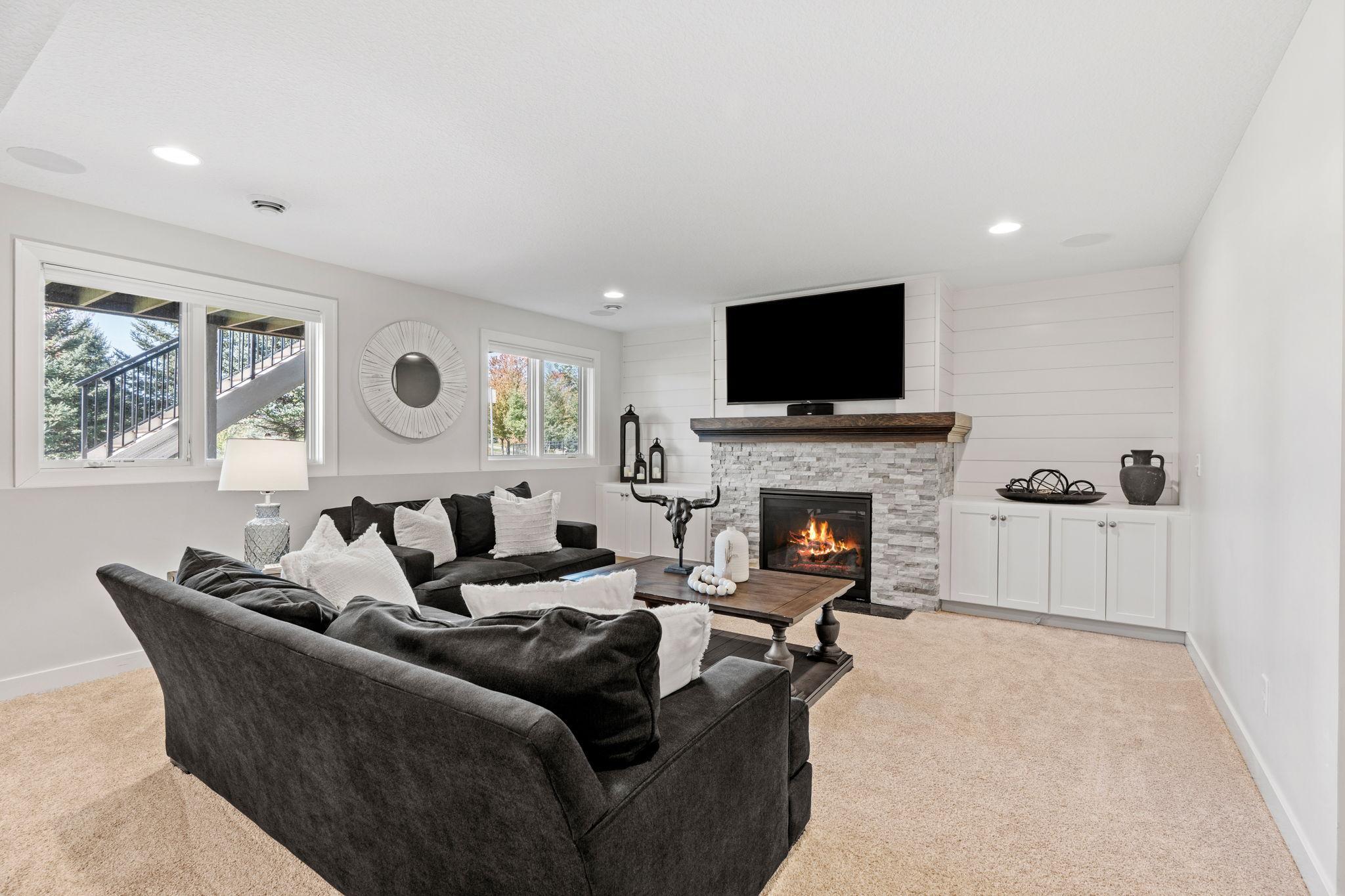Furnished living room with dark sofas, a stone fireplace, and a wall-mounted television.