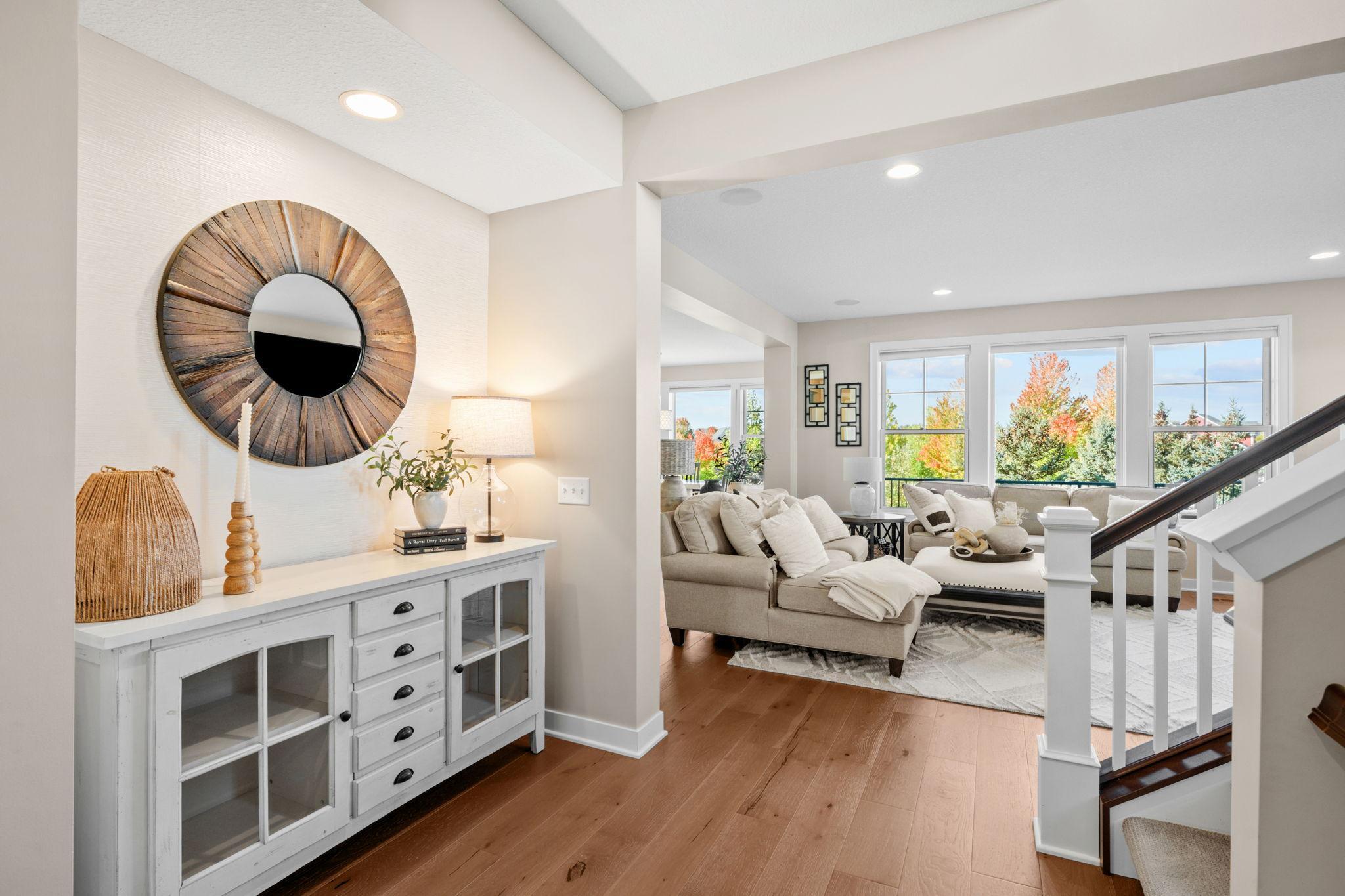 Bright foyer with warm wood floors and a white console, opening onto a cream-furnished living room.