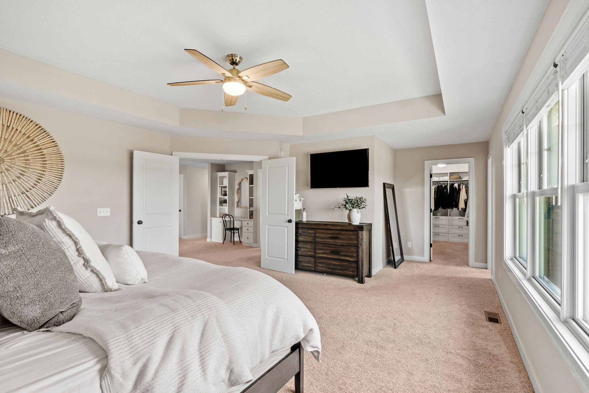 Bedroom with a white bed, ceiling fan, large windows, and a walk-in closet.