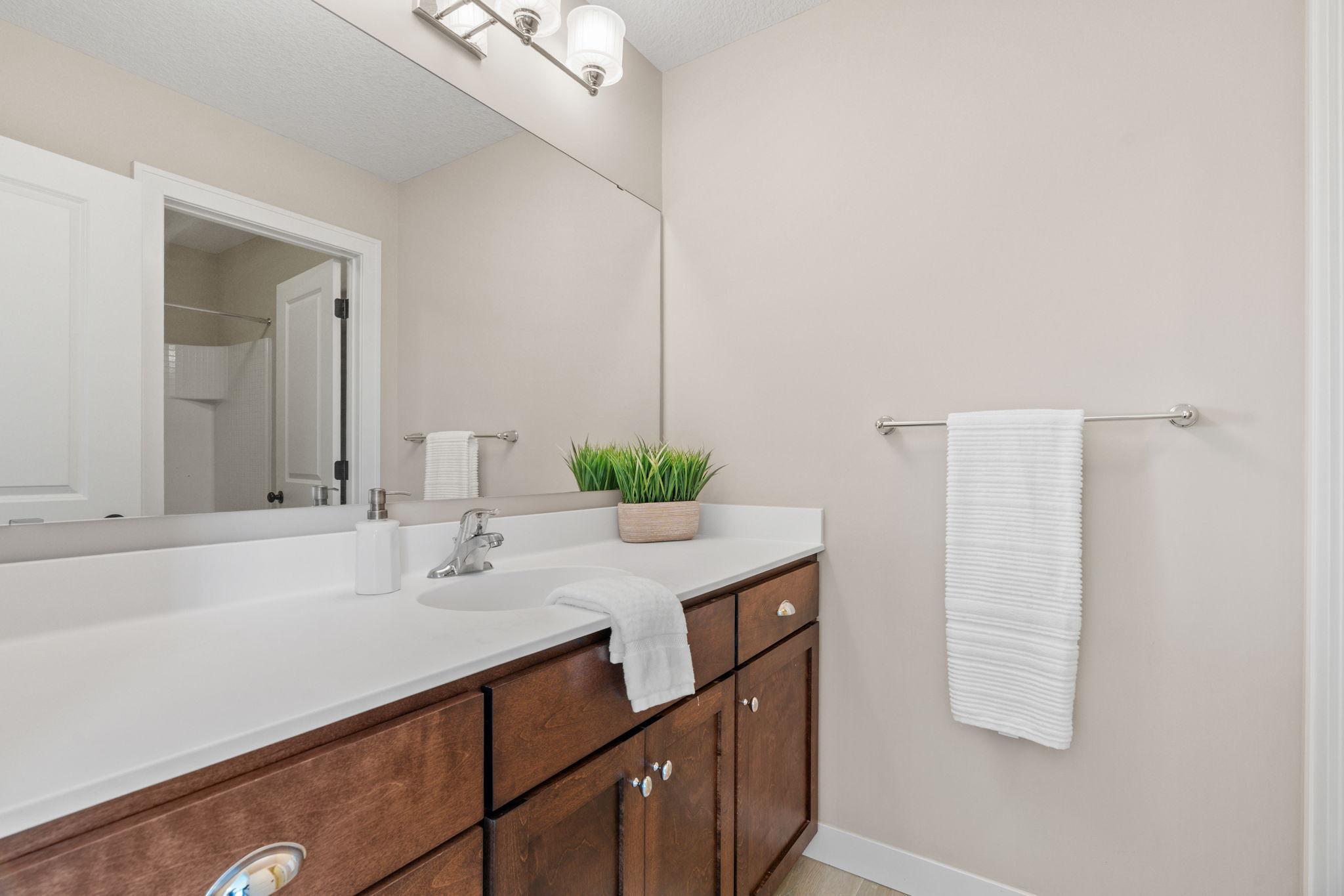 Bathroom with a dark wood vanity, long white countertop, large mirror, and tiled shower visible through the doorway.