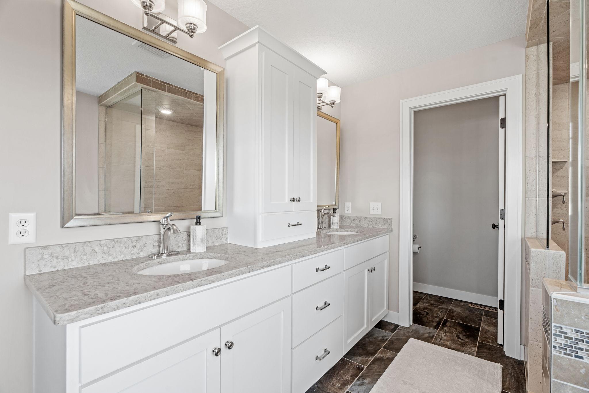 Bathroom with a white double vanity, gray stone counters, framed mirrors, and a glass-enclosed tiled shower.