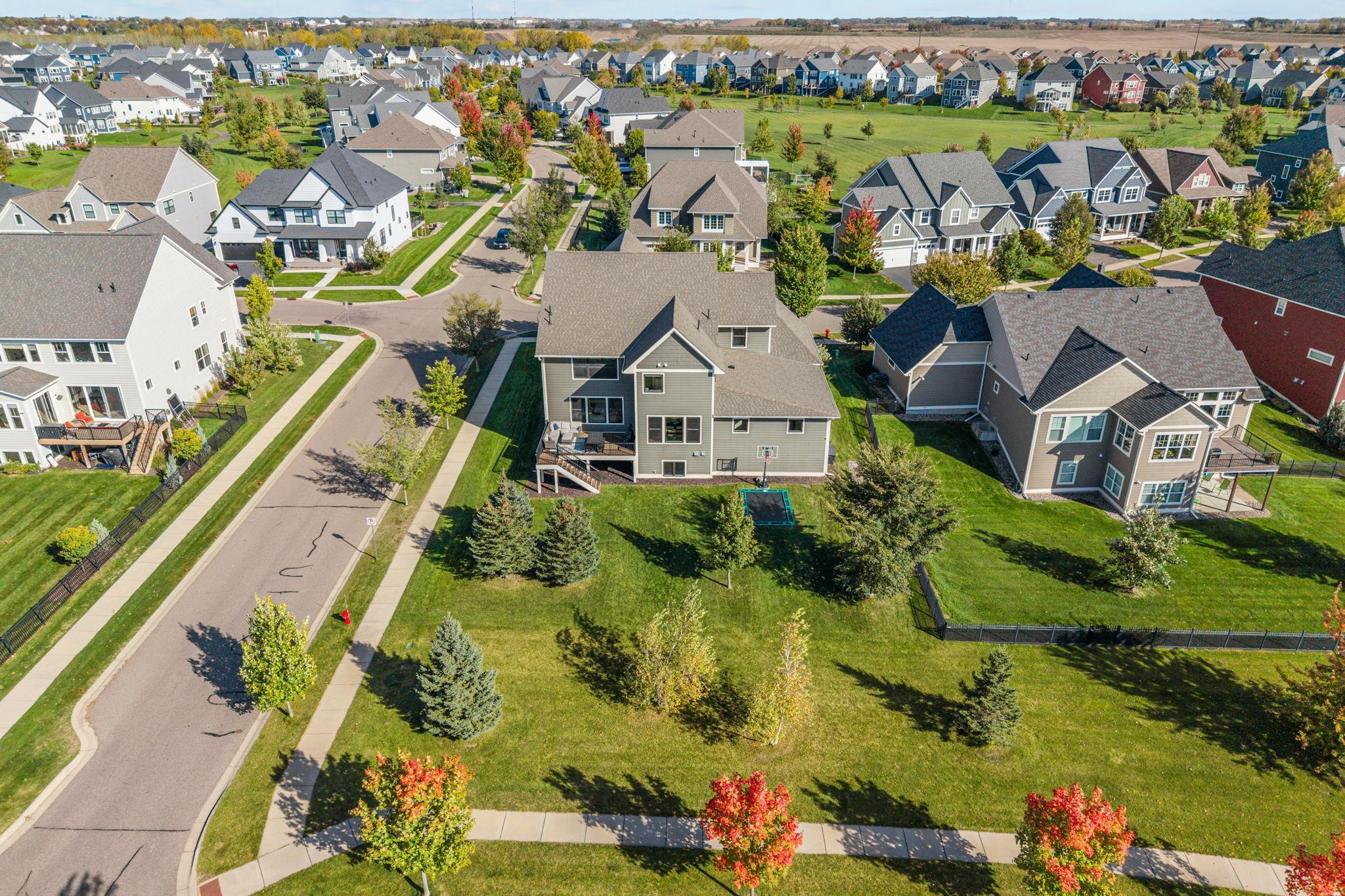 Aerial view of a gray two-story home with a deck, backyard basketball hoop, and neighboring houses.